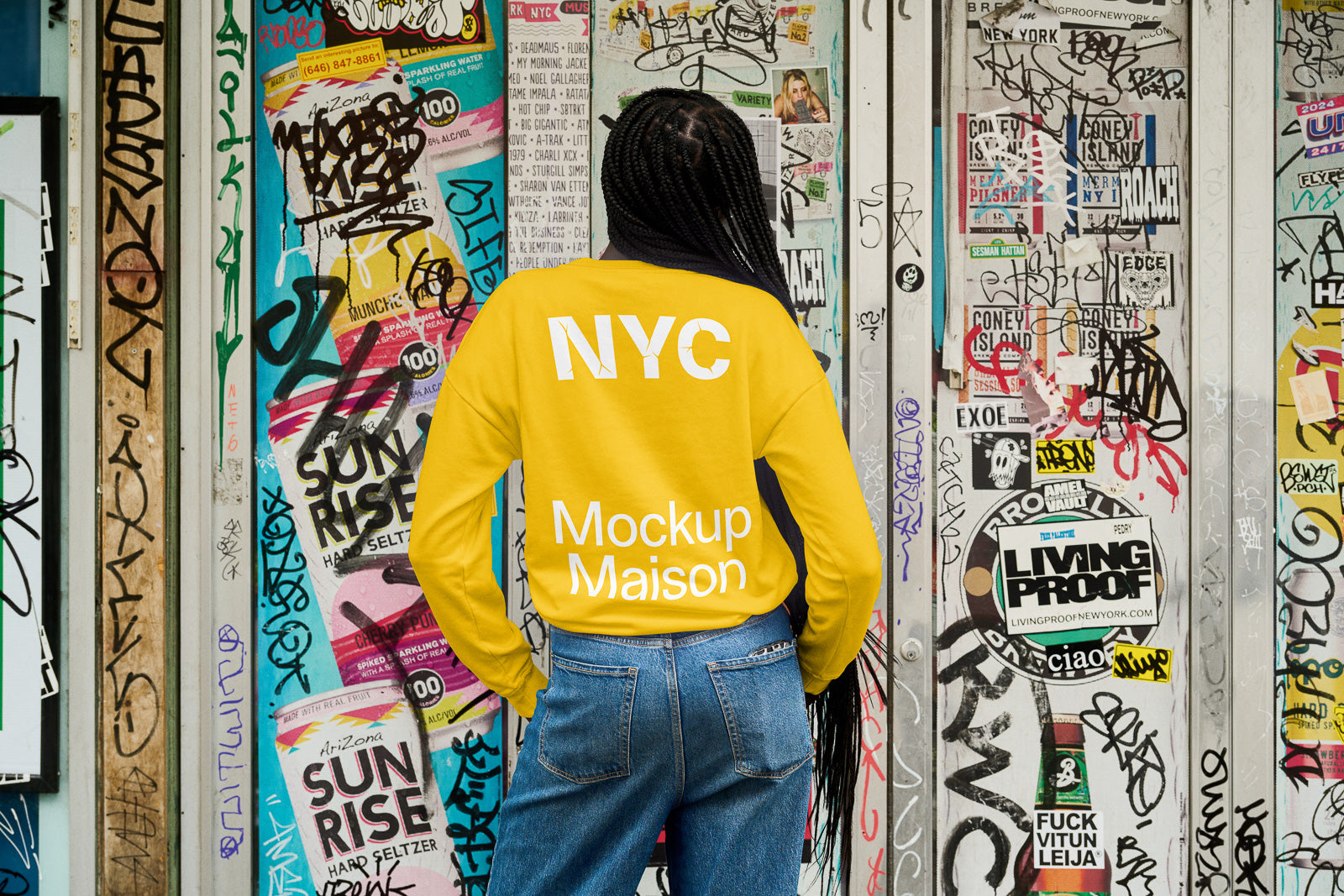 PSD mockup of person wearing a yellow sweatshirt with "NYC Mockup Maison" text, standing against a graffiti-covered wall.