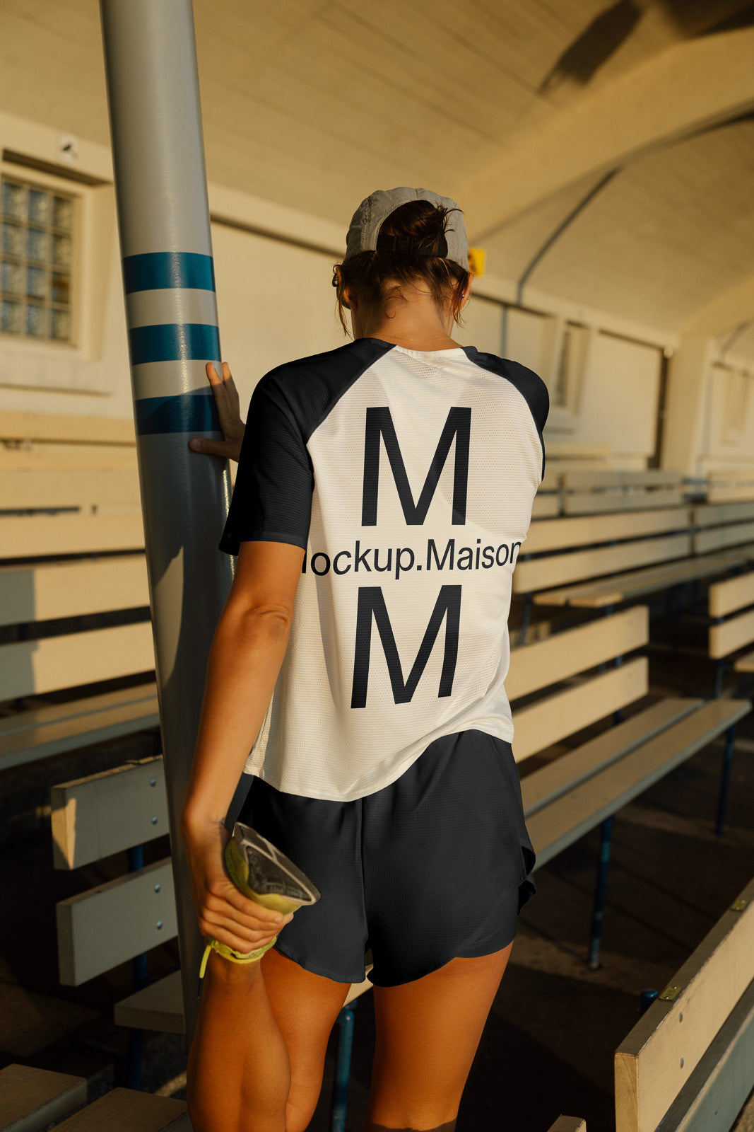 PSD mockup of a woman in a sports outfit stretching her leg on bleachers, showcasing a shirt with "Mockup.Maison" text on the back.