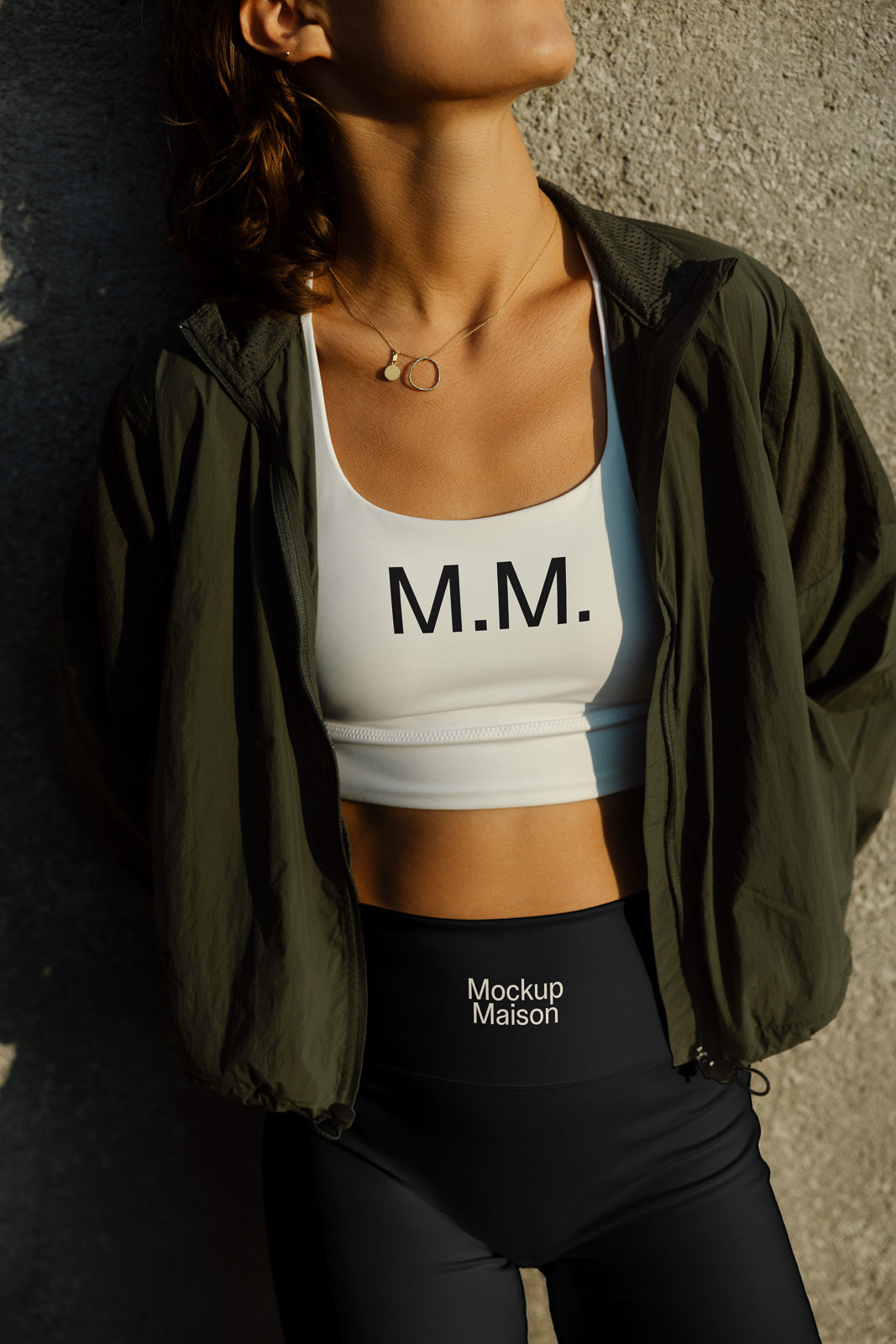 PSD mockup of a person wearing an athletic outfit, featuring a white sports bra with "M.M." and black leggings with "Mockup Maison" text under a green jacket.