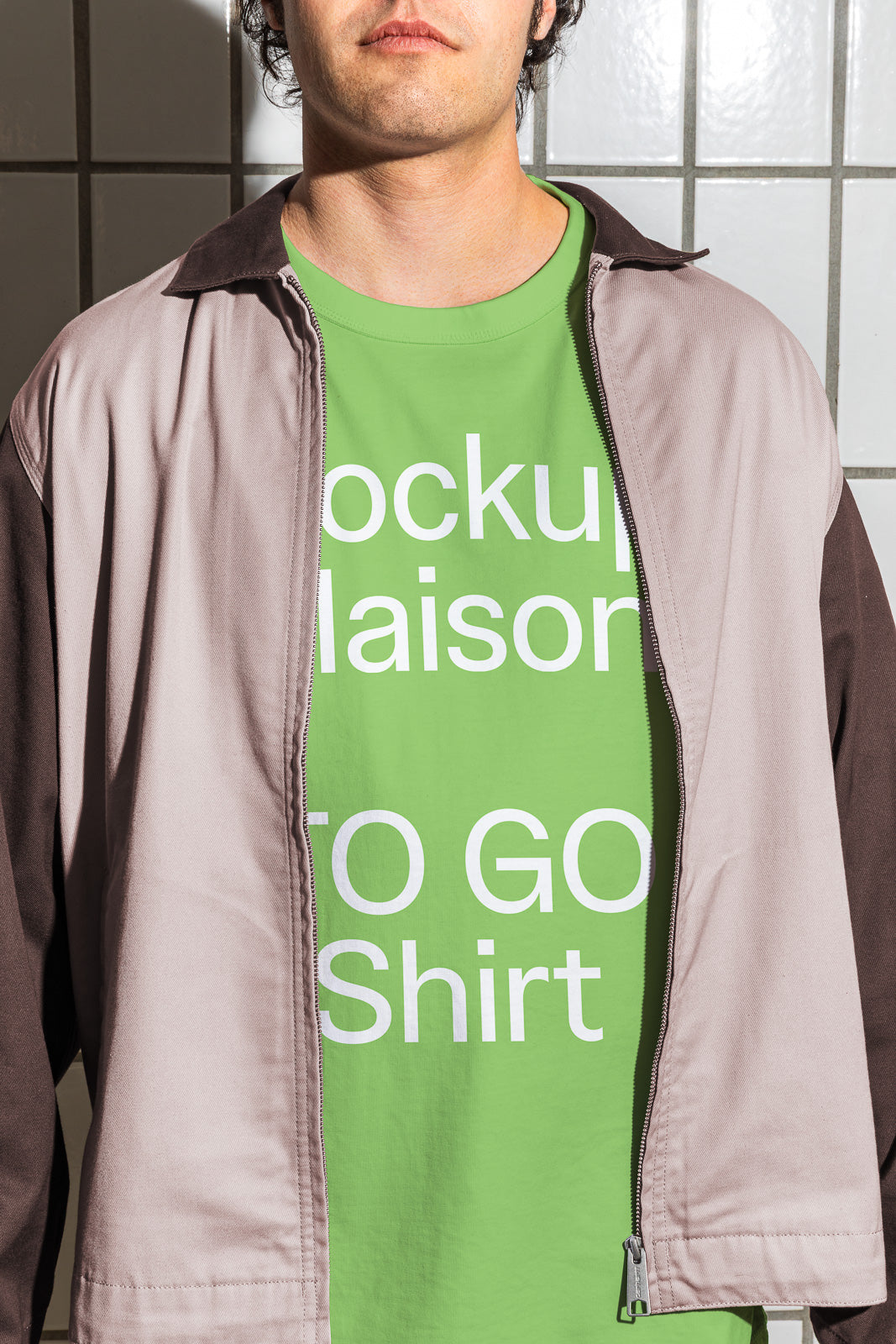 PSD mockup of a person wearing a light jacket over a green shirt with bold white text, standing against a tiled wall.