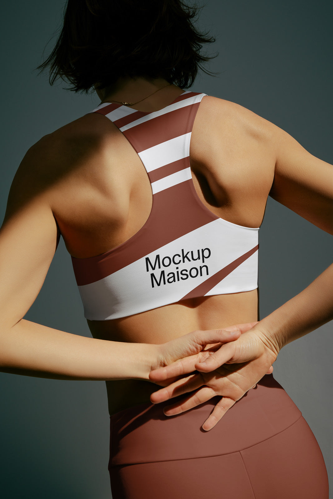 PSD mockup of a woman's back wearing a brown and white sports bra with "Mockup Maison" text, hands clasped behind her.