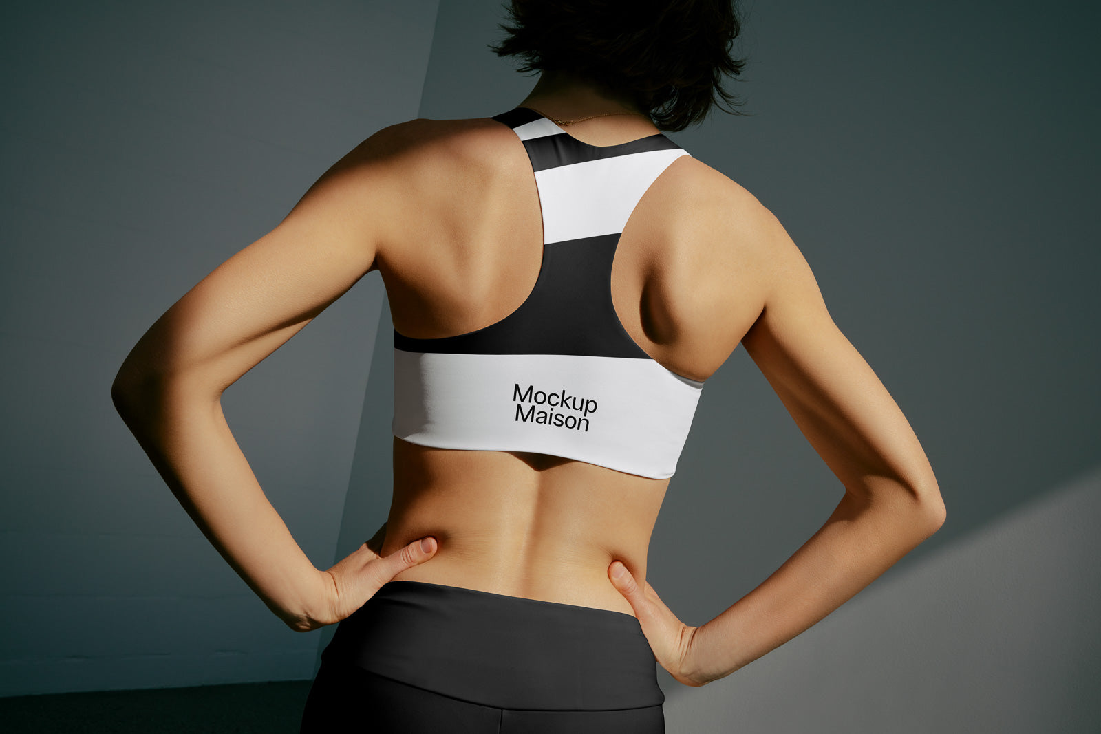 PSD mockup of a woman in a sporty black and white racerback top with "Mockup Maison" text, hands on hips, displaying athletic design.