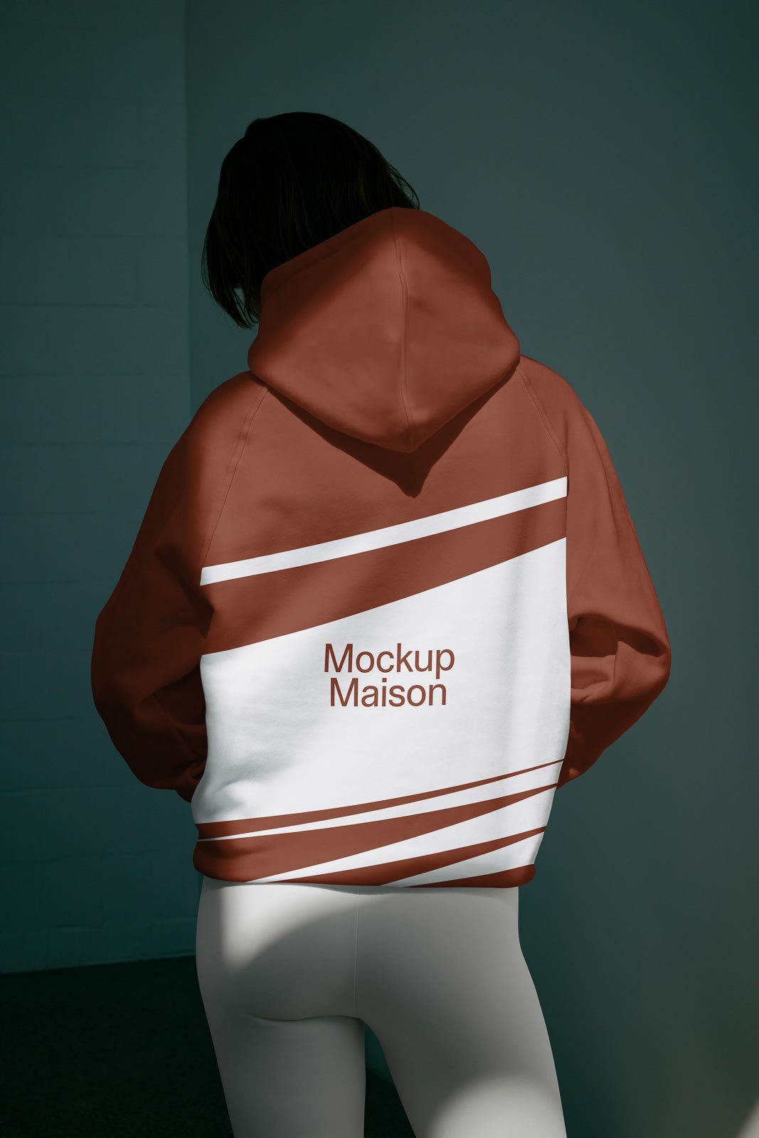 PSD mockup of a person wearing a brown hoodie with white stripes and the text "Mockup Maison" on the back. The design stands out against a dark background.