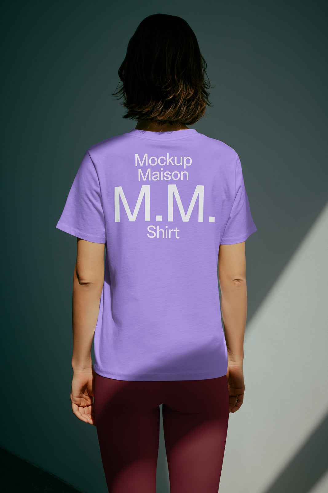 PSD mockup of a person wearing a lavender T-shirt with "Mockup Maison M.M. Shirt" in white text on the back, standing indoors.