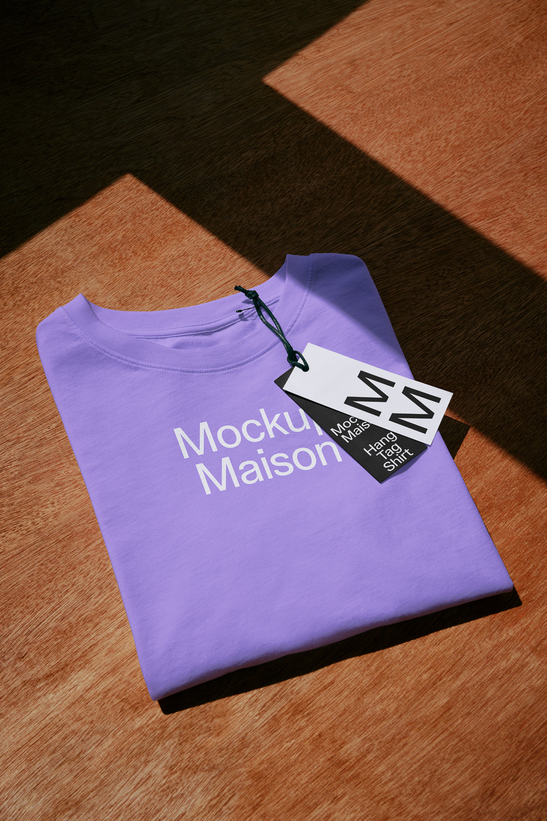 PSD mockup of a folded purple t-shirt with "Mockup Maison" text, featuring a double tag on a wooden surface with sunlight casting shadows.