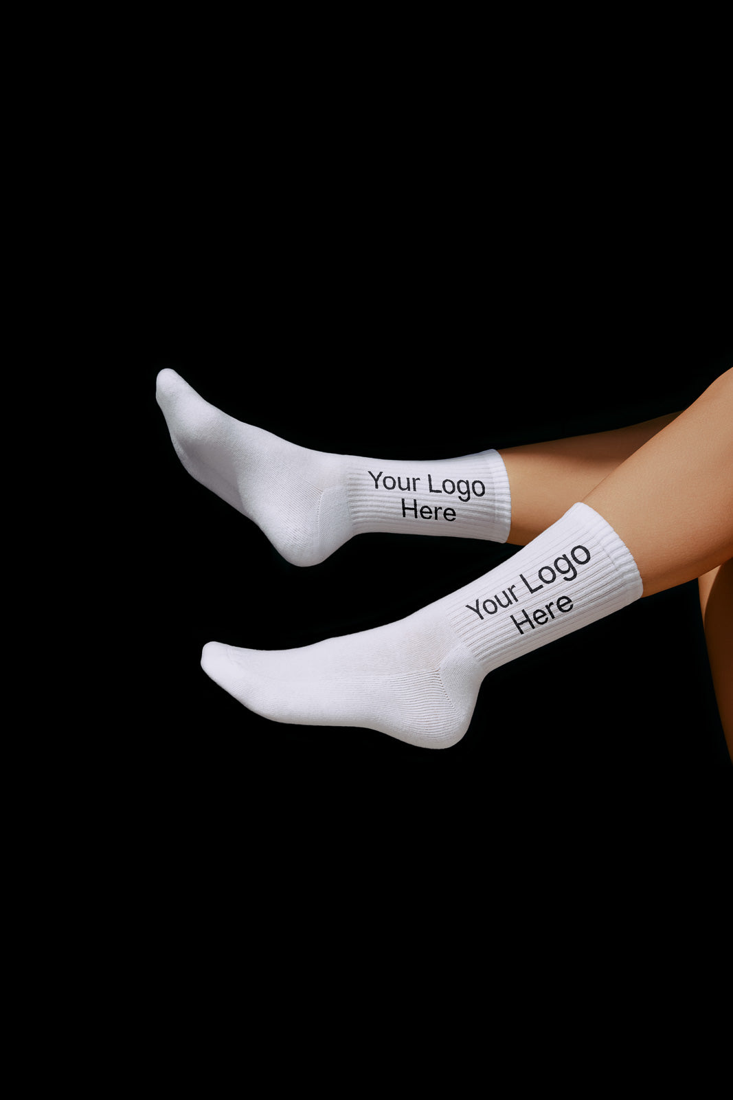 PSD mockup of white socks with "Your Logo Here" text on the sides, displayed on a black background to highlight customizable design placement.