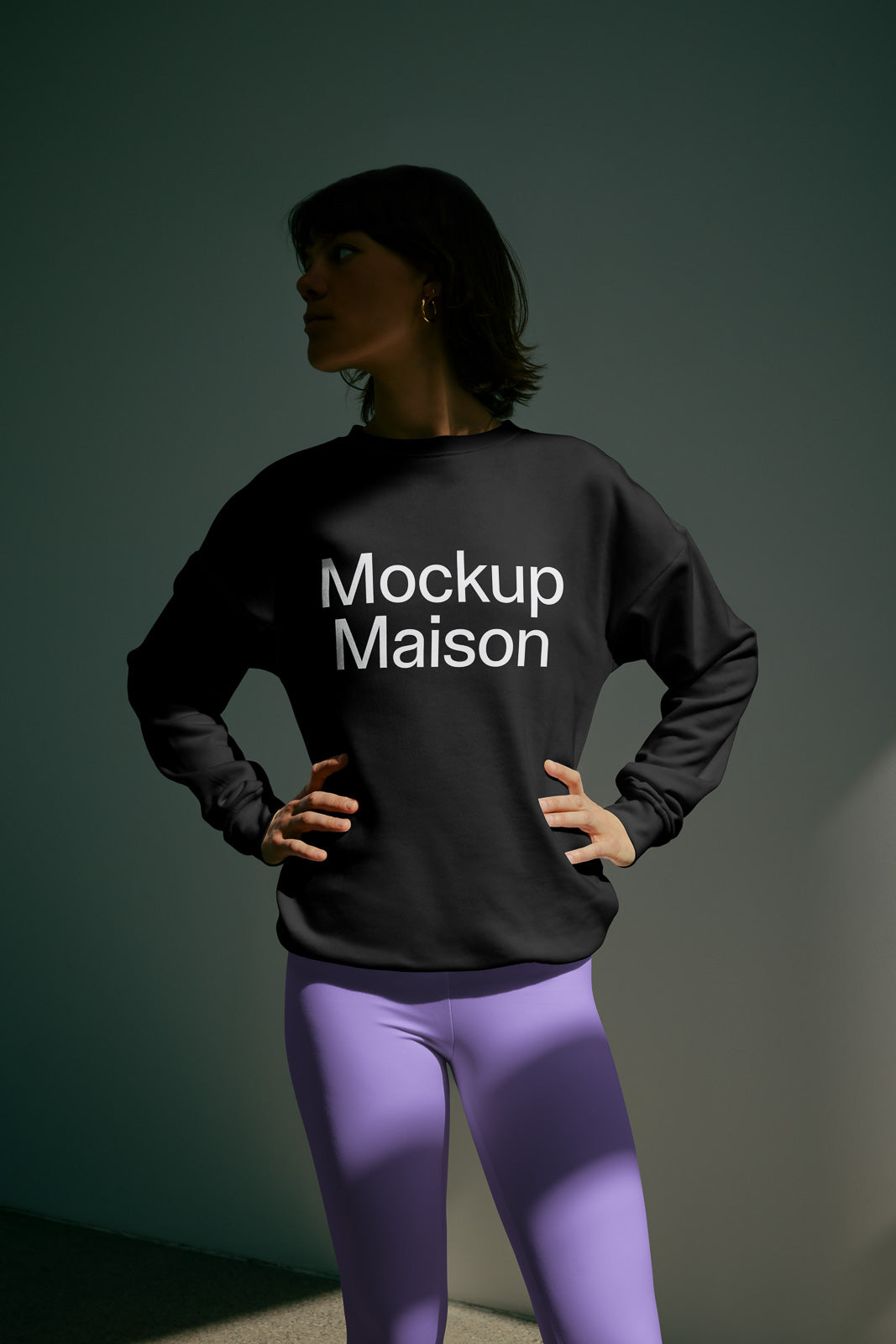 PSD mockup of a person in a black sweatshirt with "Mockup Maison" text, paired with purple leggings, standing hands on hips in soft lighting.