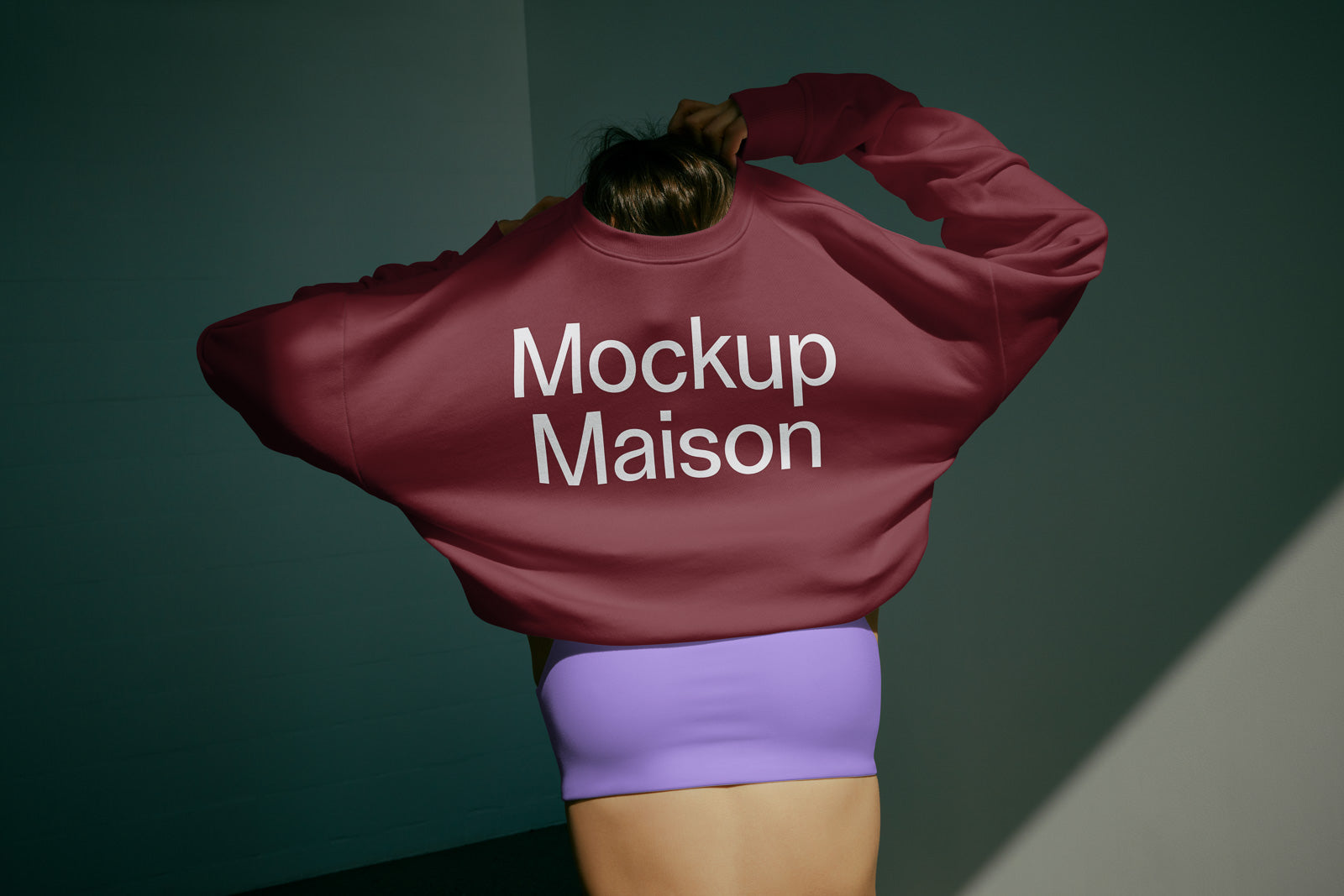 PSD mockup of a person wearing a maroon sweatshirt with "Mockup Maison" text, paired with purple bottoms, in an indoor setting.