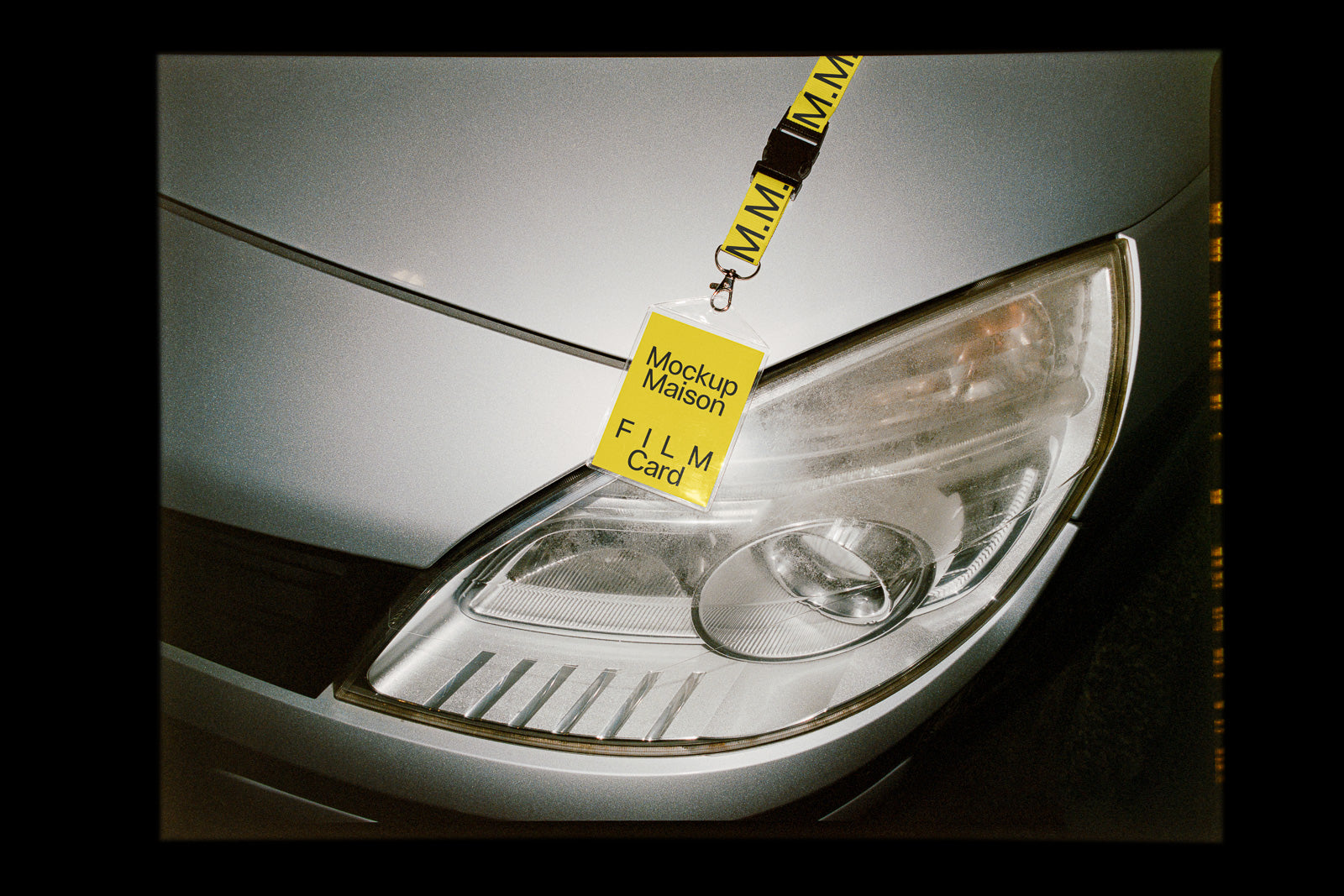 PSD mockup of a yellow lanyard with attached card, placed on a silver car hood near the headlight. The card reads "Mockup Maison FILM Card."