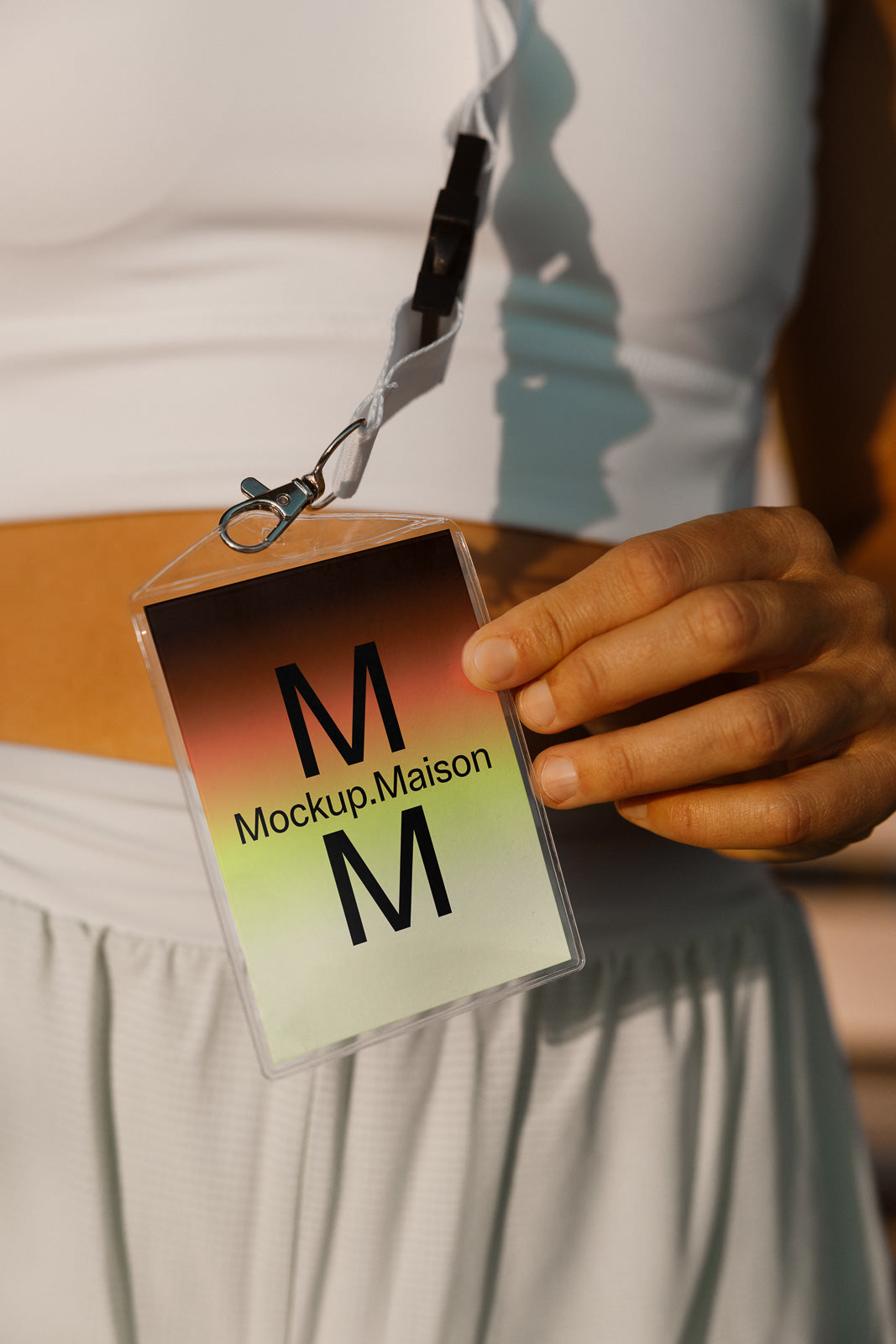PSD mockup of a hand holding a lanyard with a badge displaying "Mockup.Maison" and large "M" letters against a gradient background.