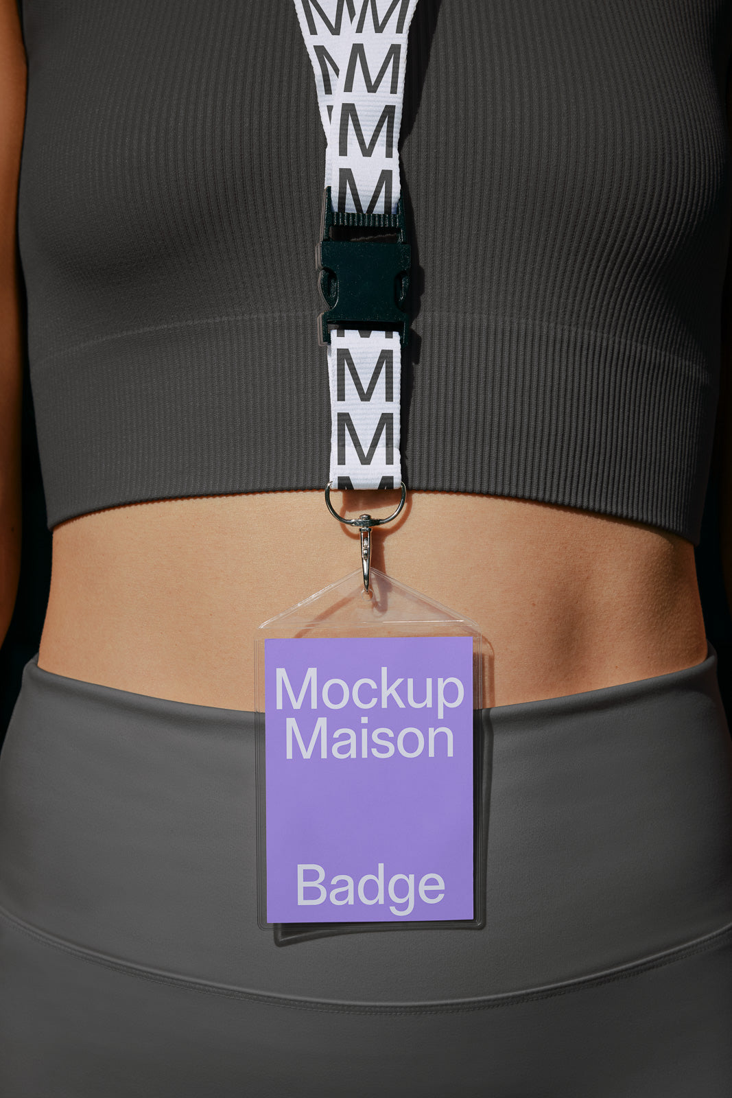 PSD mockup of a waist-length view of a person wearing a lanyard with a clear badge holder displaying "Mockup Maison Badge" against a gray top.