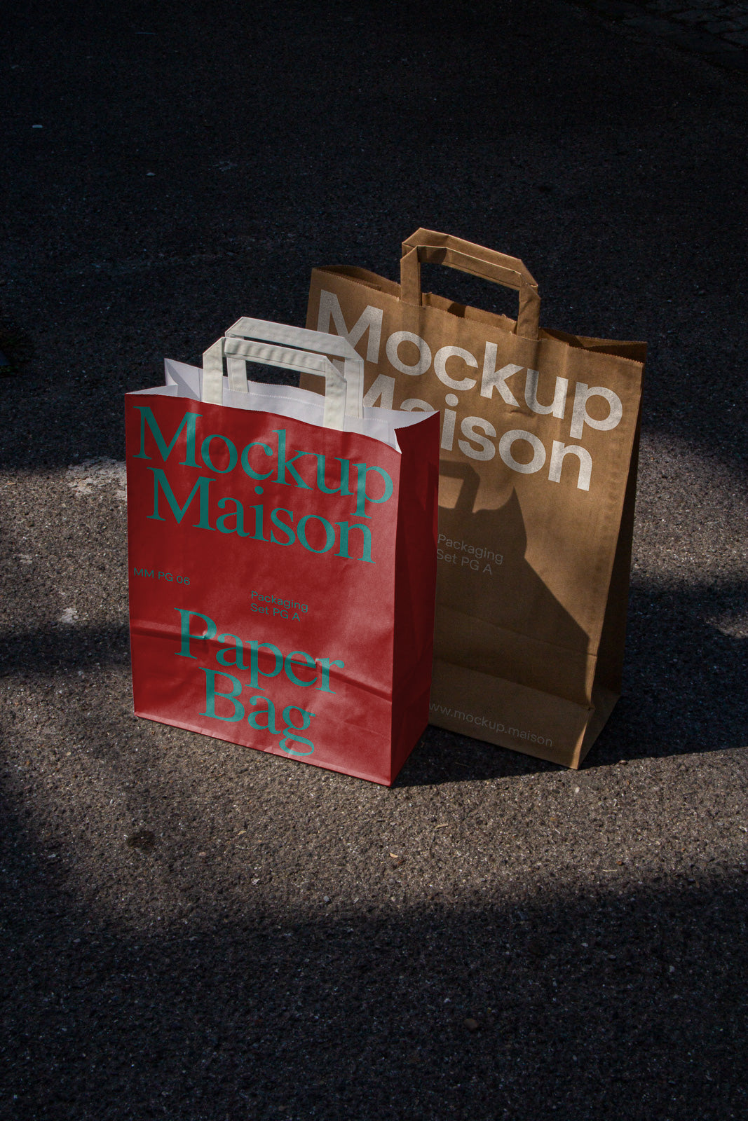 PSD mockup of two paper bags on an asphalt surface, one red with teal text "Mockup Maison Paper Bag" and one brown with white text "Mockup Maison."