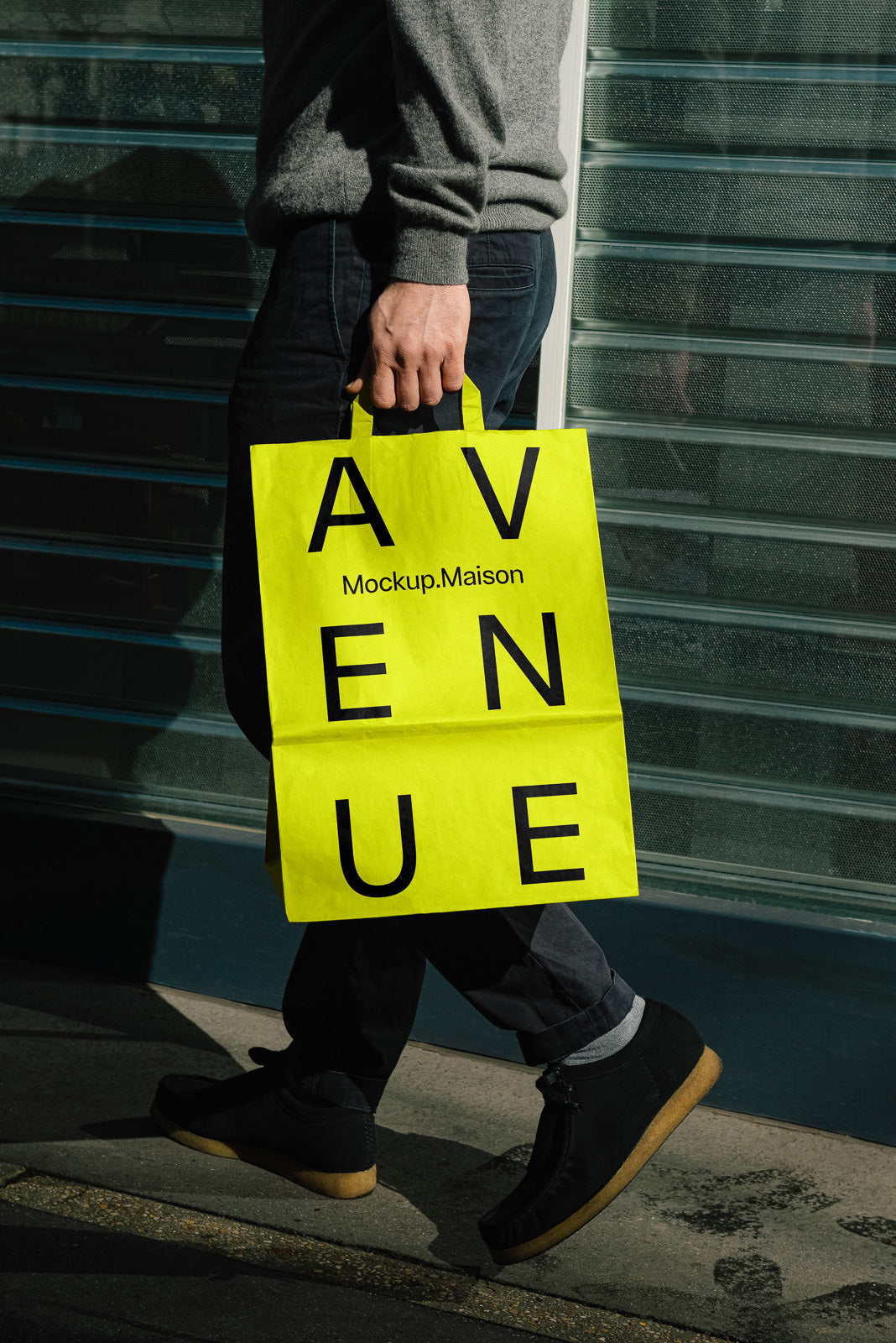 PSD mockup of a person walking with a bright yellow paper bag labeled "AVENUE" and "Mockup.Maison" against a modern building backdrop.