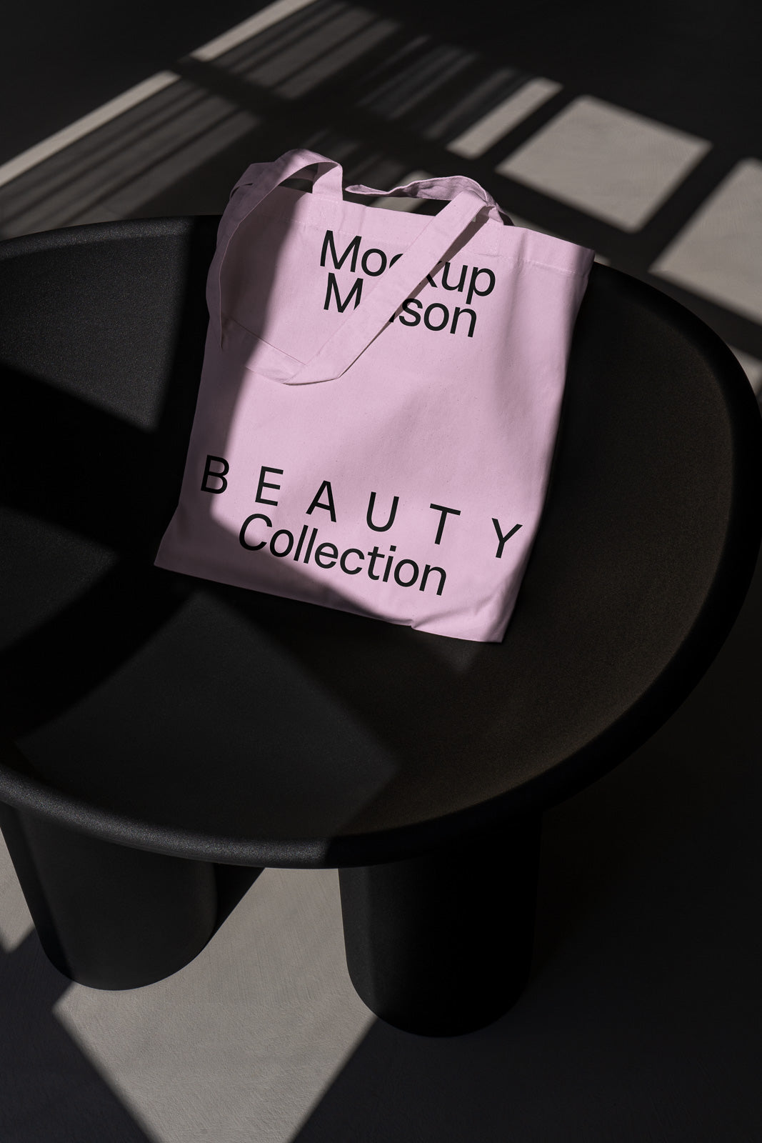 PSD mockup of a pink tote bag with "Mockup Mason" and "BEAUTY Collection" text, placed on a dark modern chair under a patterned shadow.