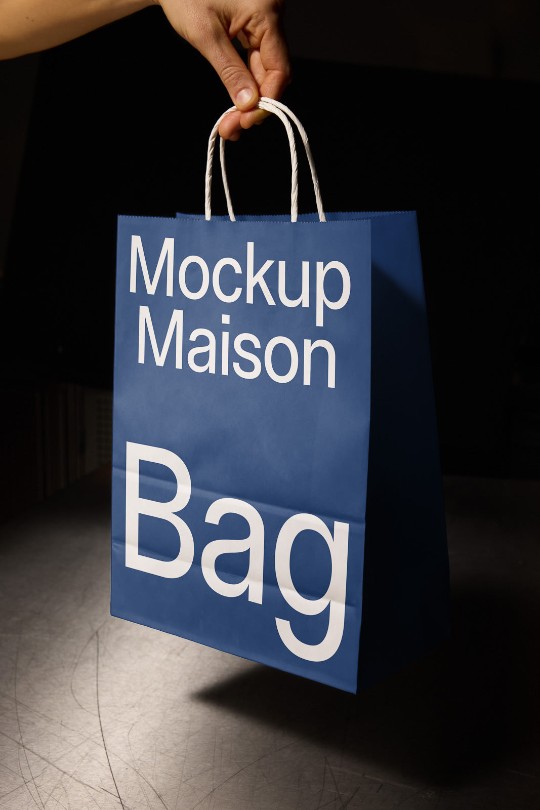 PSD mockup of a blue shopping bag with "Mockup Maison Bag" text held by a hand against a dark background.