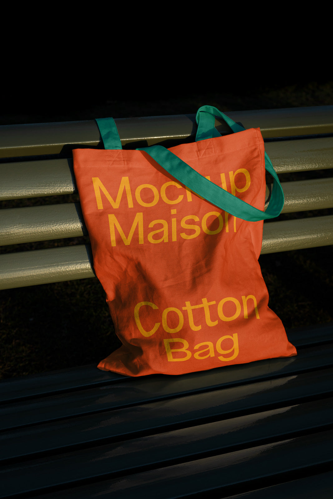 PSD mockup of an orange cotton tote bag with yellow text and green handles, resting on a bench in sunlight, showcasing branding design.