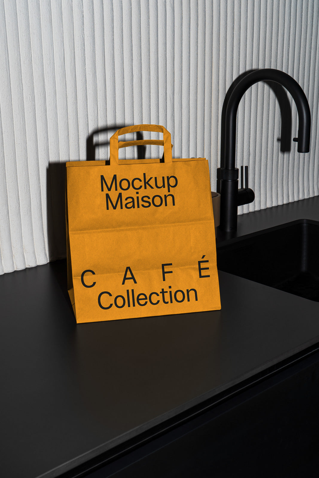 PSD mockup of an orange paper bag with "Mockup Maison" and "Café Collection" text, placed on a dark countertop near a black faucet.