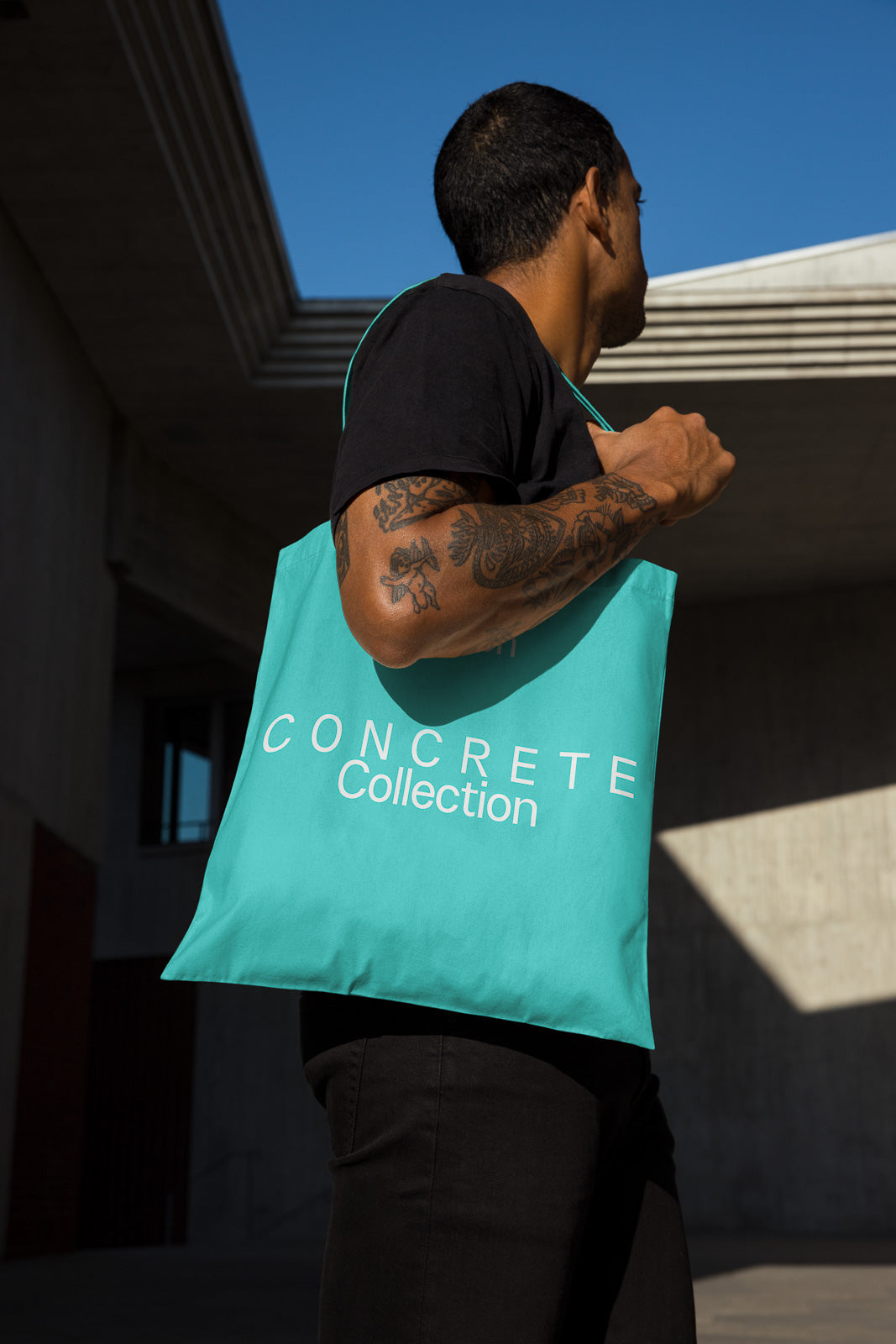 PSD mockup of a person holding a turquoise tote bag with "Concrete Collection" text, set against an urban background with modern architecture.
