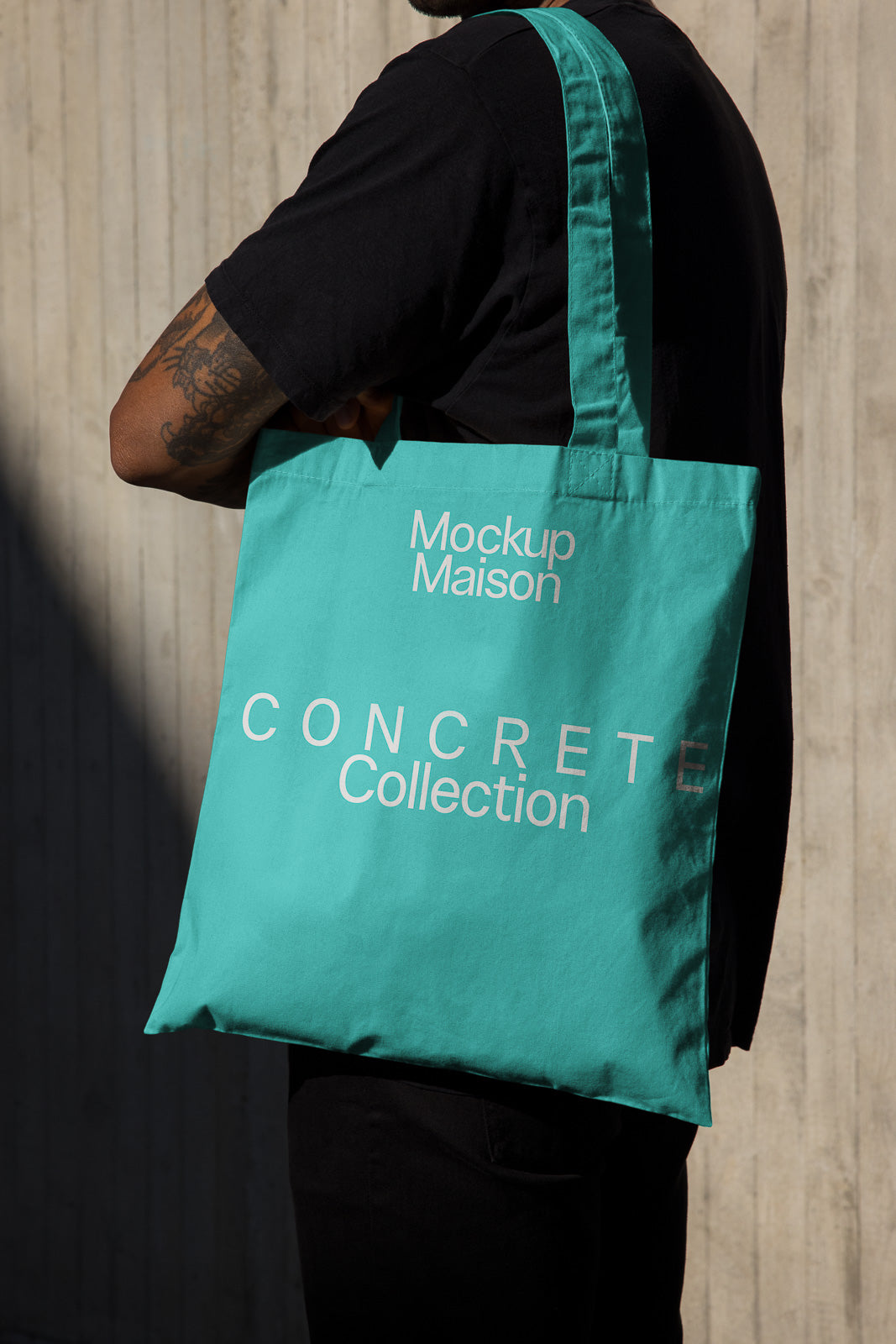 PSD mockup of a person holding a teal tote bag featuring "Mockup Maison" and "Concrete Collection" text, with a concrete wall background.