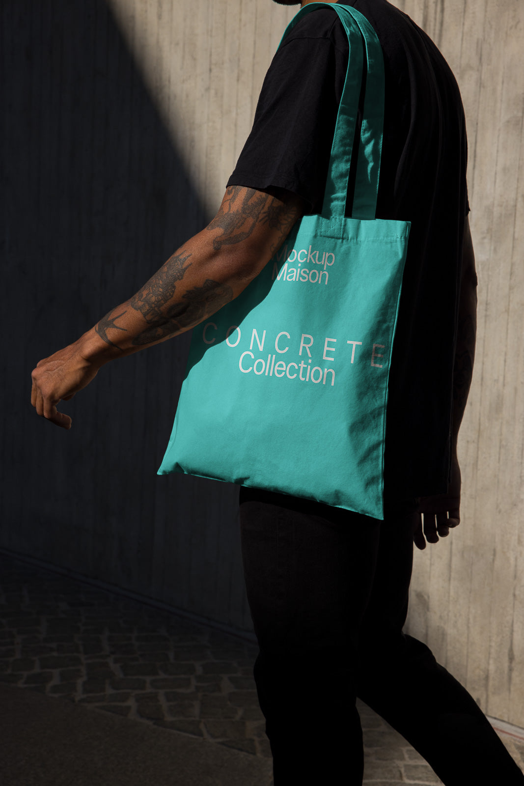 PSD mockup of a person carrying a turquoise tote bag with "CONCRETE Collection" text, highlighting the bag's design alongside a shadowed concrete wall.