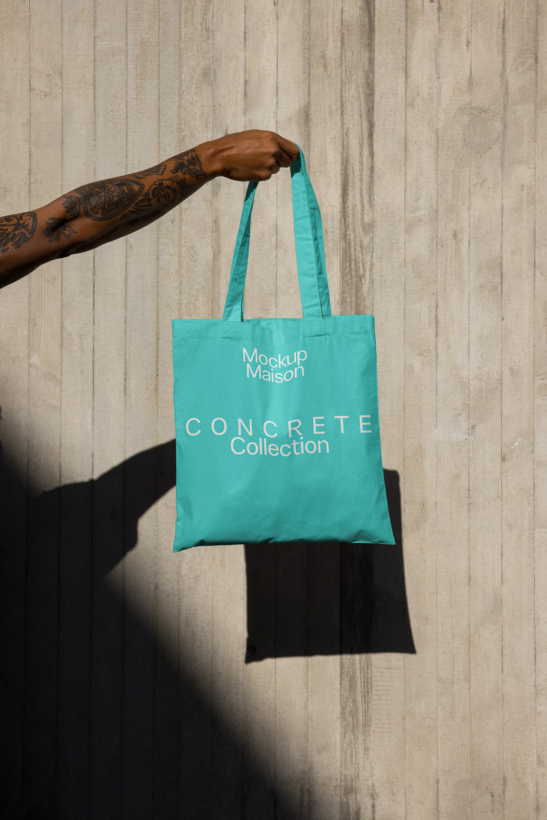 PSD mockup of a person holding a turquoise tote bag against a concrete wall, featuring the "Concrete Collection" and "Mockup Maison" text.