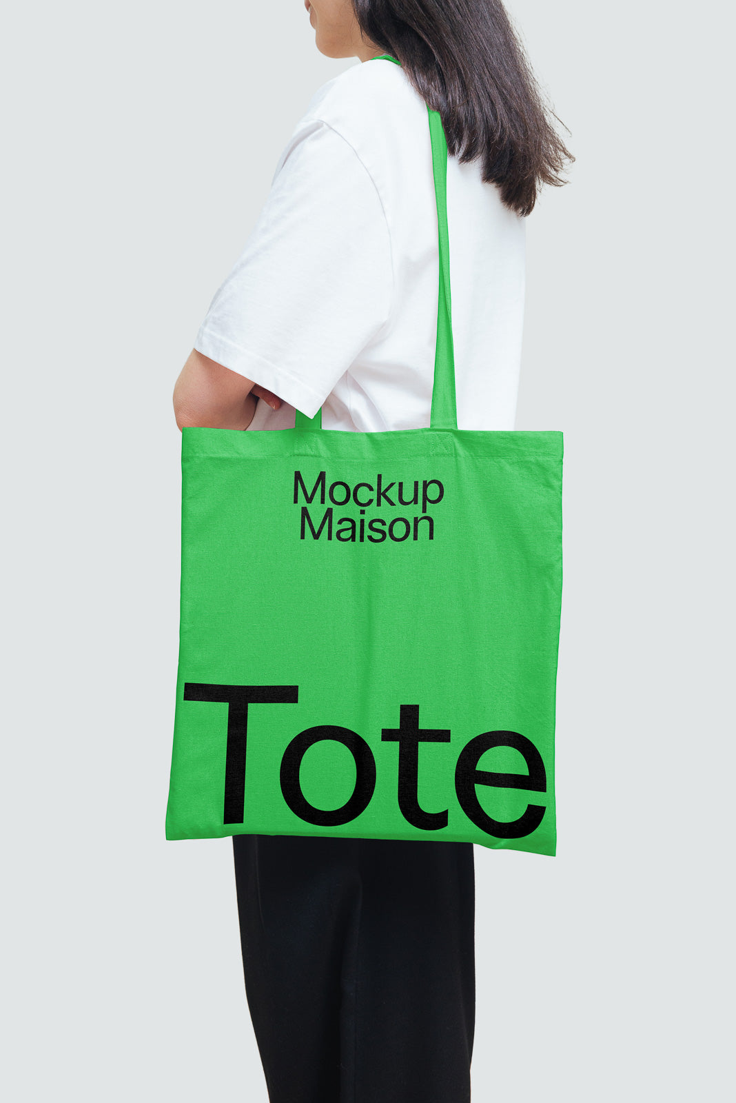 PSD mockup of a green tote bag with bold black text, "Mockup Maison Tote," carried by a person in a white shirt, against a plain background.