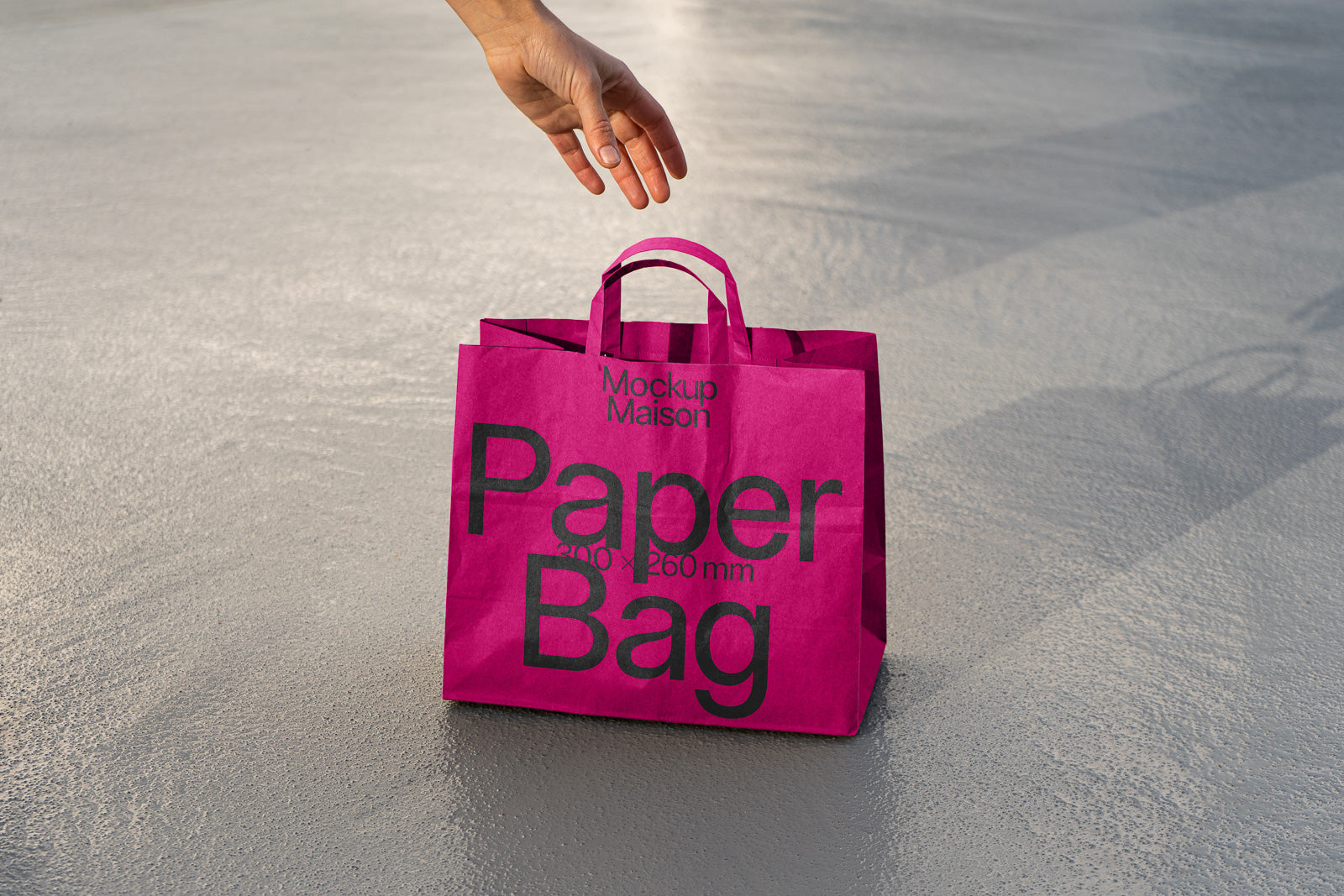 PSD mockup of a pink paper bag with black text, featuring a hand reaching towards it on a textured gray surface.
