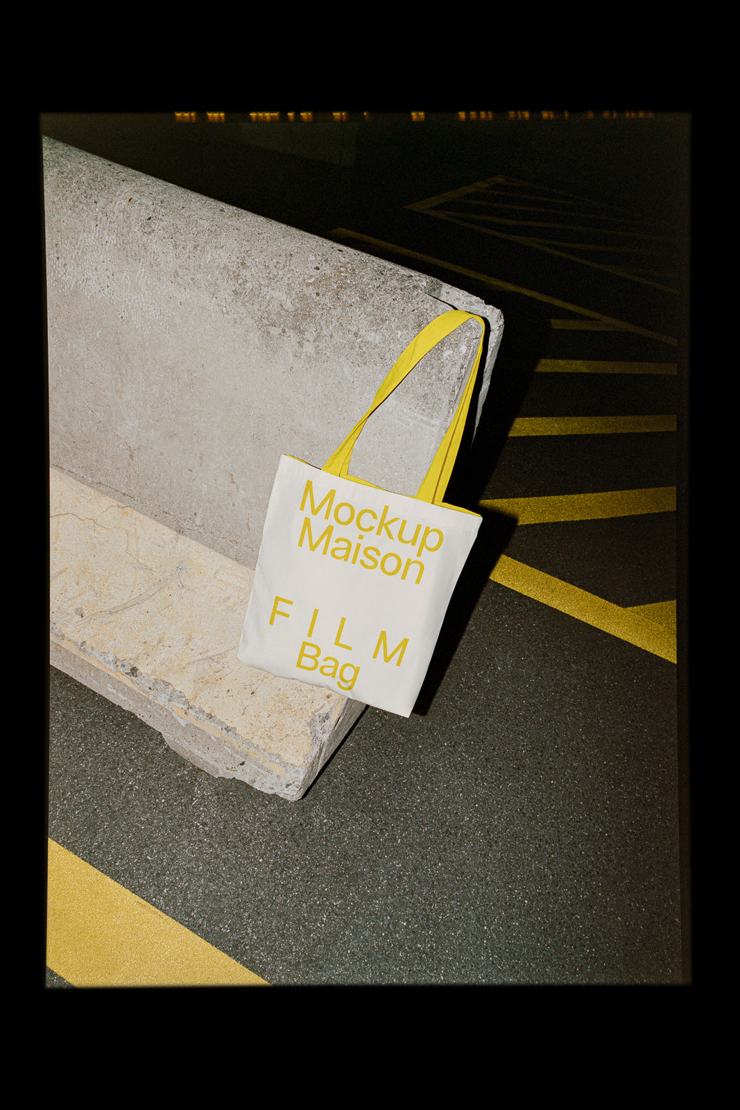 PSD mockup of a tote bag with "Mockup Maison FILM Bag" text, featuring yellow handles. The bag is placed against a concrete surface on an urban street.