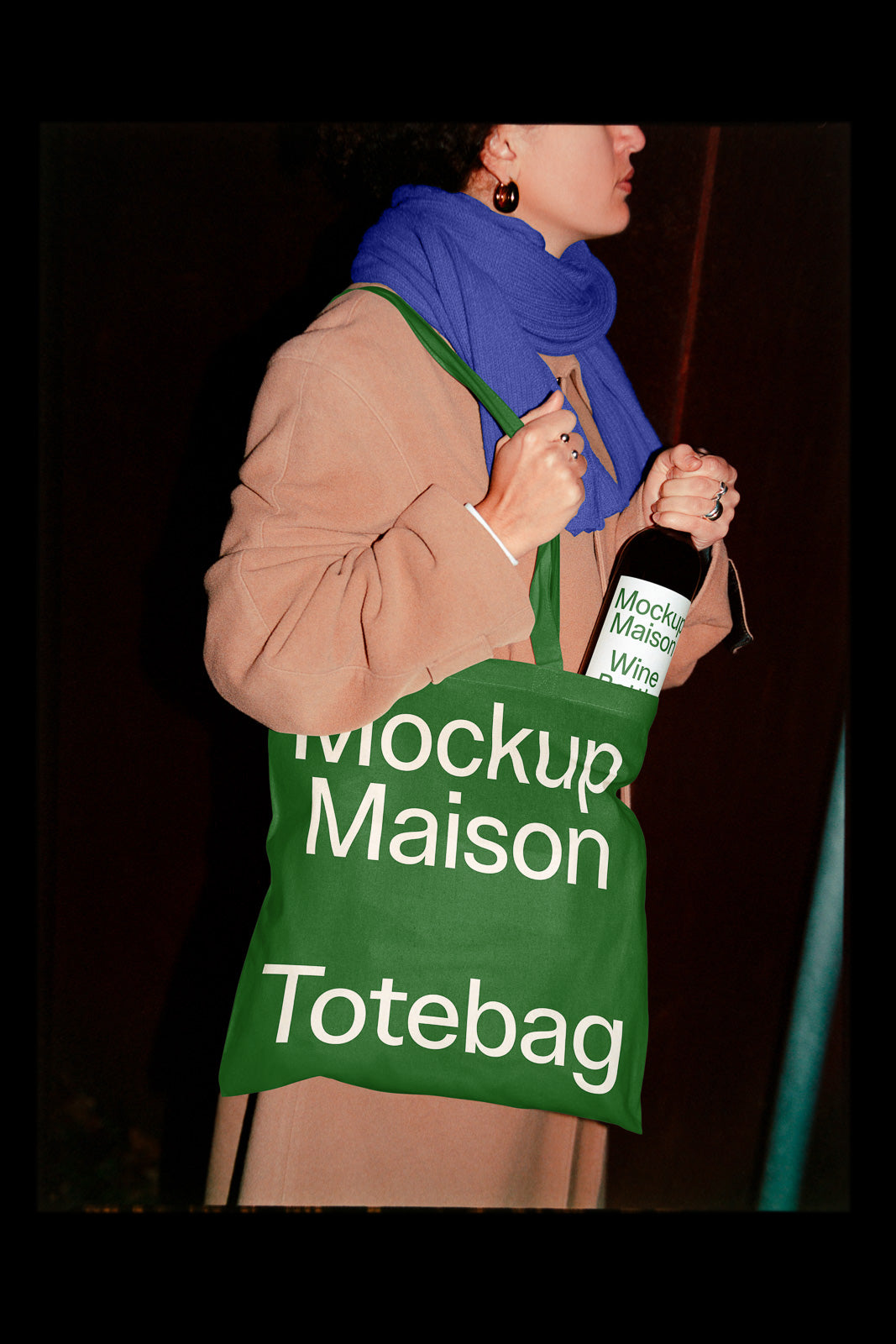 PSD mockup of a person holding a green tote bag with the text "Mockup Maison Totebag" and a matching wine bottle in hand, wearing a blue scarf.