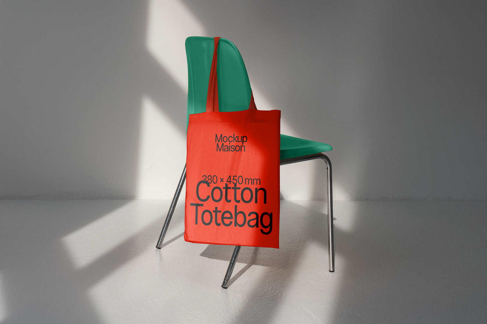 PSD mockup of a red cotton tote bag hanging on a green chair, displaying text "Mockup Maison" and "380 x 450 mm Cotton Totebag" in a sunlit room.