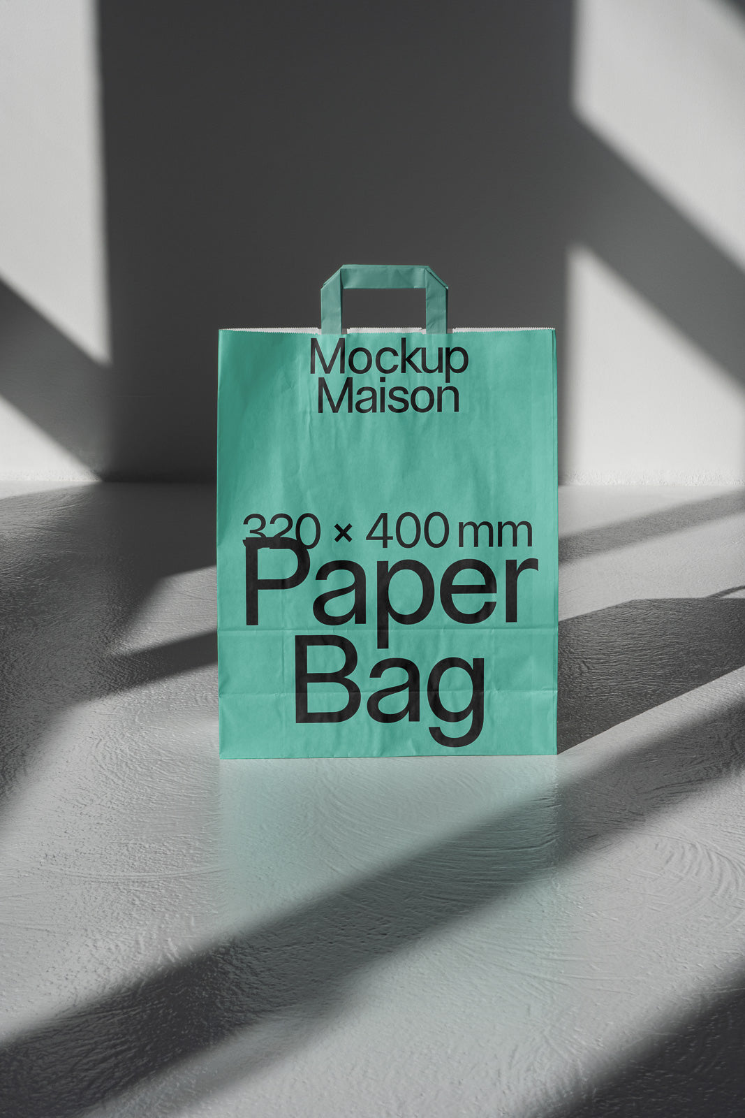 PSD mockup of a teal paper bag with the text "Mockup Maison" and "320 x 400 mm Paper Bag" on a textured surface with shadows.