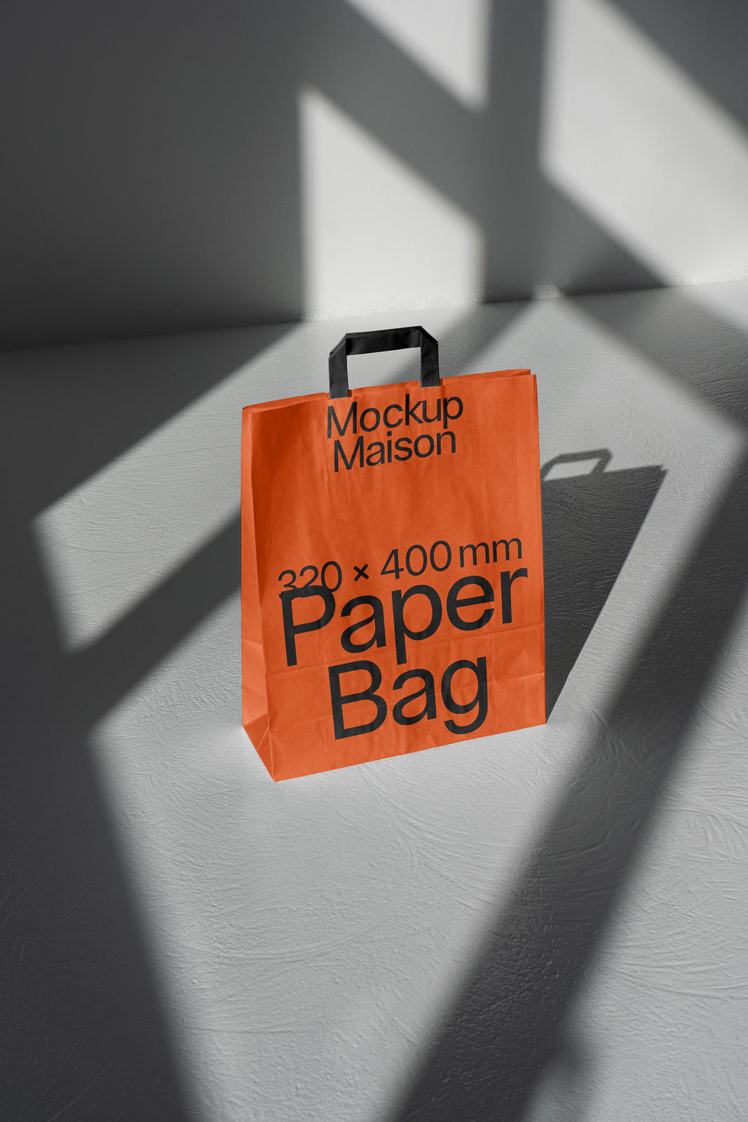 PSD mockup of an orange paper bag with black handles, labeled "Mockup Maison 320 × 400 mm Paper Bag," placed on a textured surface with shadows.