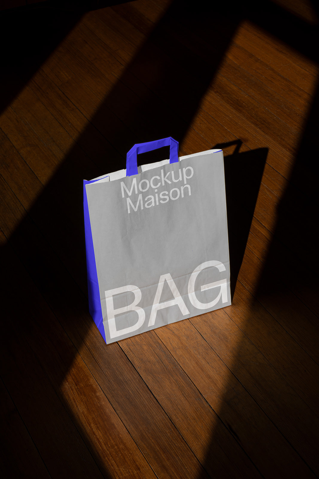PSD mockup of a paper shopping bag with blue handles on a wooden floor, featuring the text "Mockup Maison BAG" in large, bold letters.