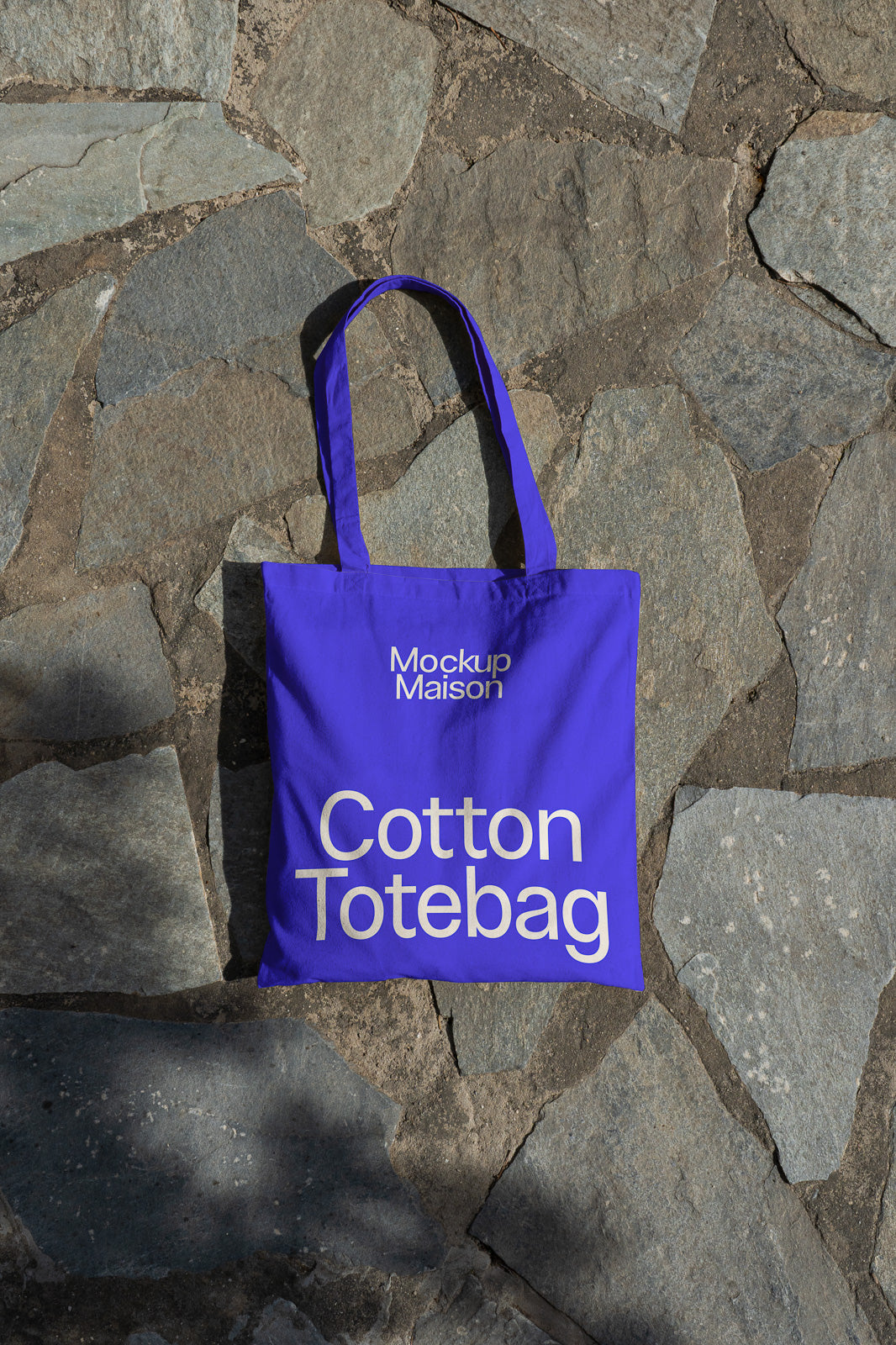 PSD mockup of a blue cotton tote bag with "Mockup Maison" text, placed on a textured stone background for a realistic presentation.