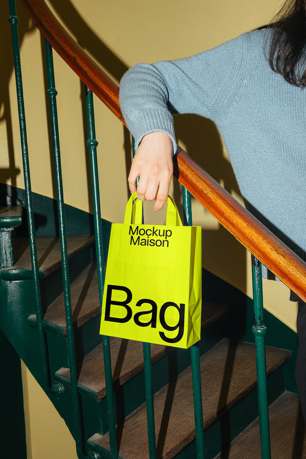 PSD mockup of a bright yellow paper bag with bold black lettering held by a person on a staircase, emphasizing modern design elements.