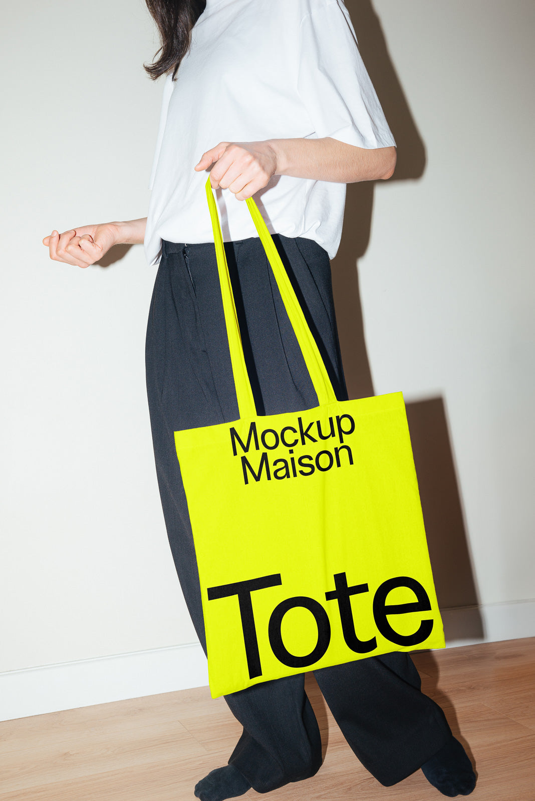 PSD mockup of a person holding a bright yellow tote bag with "Mockup Maison" and "Tote" text, wearing a white shirt and black pants.