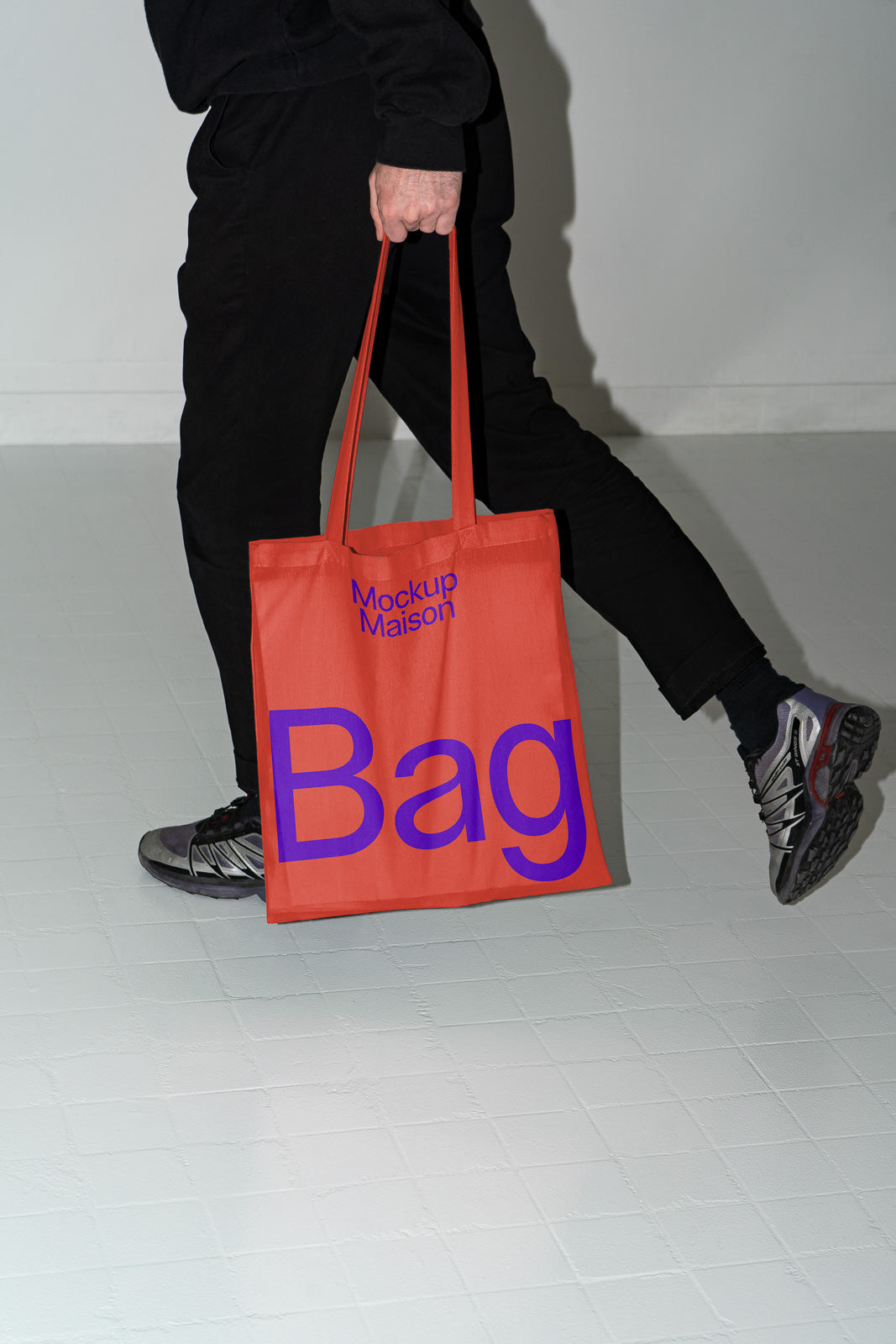 PSD mockup of a person holding an orange tote bag with purple text "Mockup Maison Bag" against a plain background.