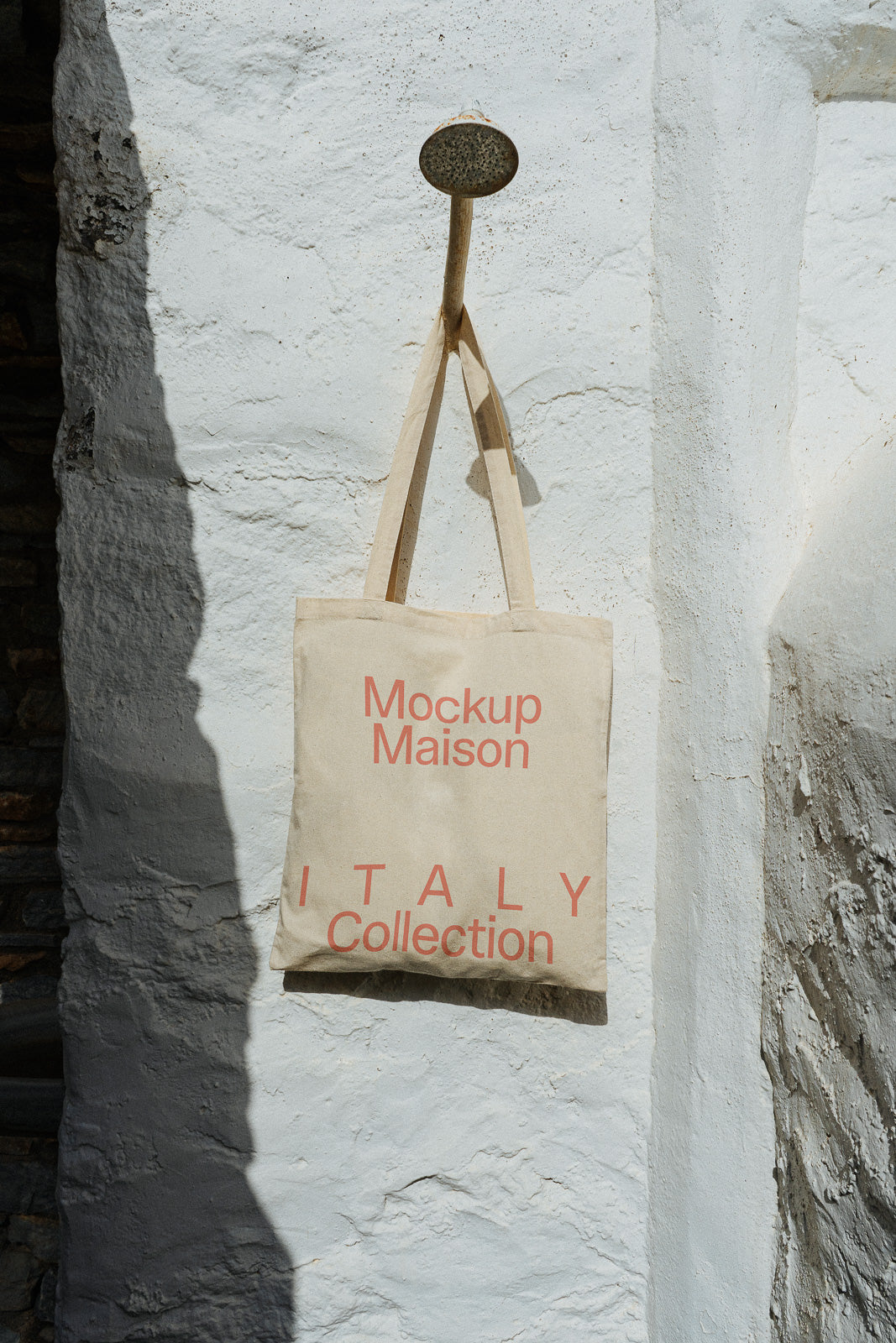 PSD mockup of a canvas tote bag hanging on a rustic white wall, labeled "Mockup Maison Italy Collection" in red text.