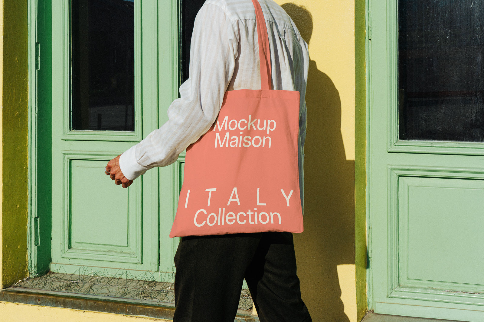 PSD mockup of a person carrying a pink tote bag with "Mockup Maison ITALY Collection" text, standing against a yellow wall and green door.