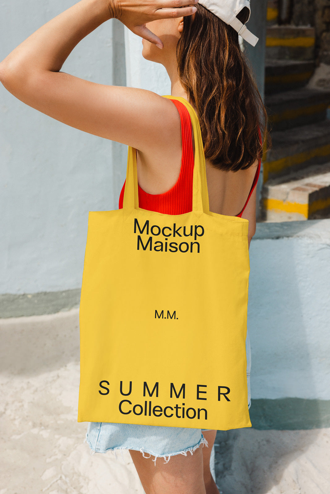 PSD mockup of a woman holding a yellow tote bag with "Mockup Maison," "M.M.," and "Summer Collection" text, wearing a red tank top and white cap.