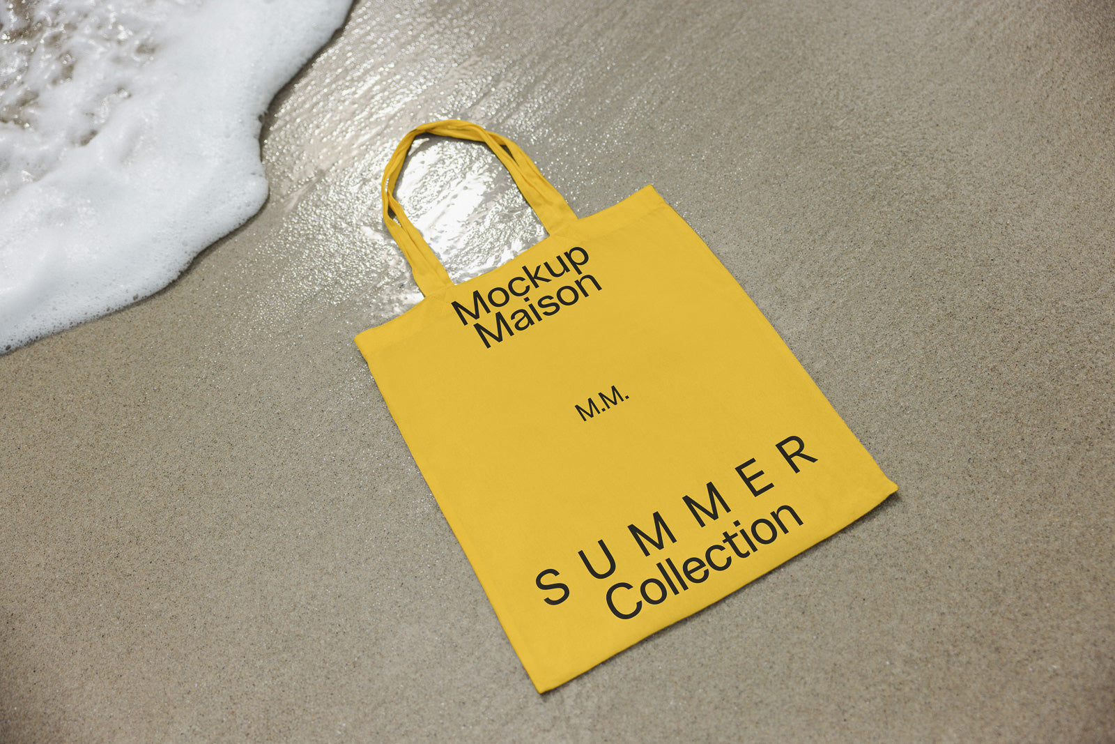 PSD mockup of a yellow tote bag with "Mockup Maison" and "Summer Collection" text, placed on wet sand near ocean waves.
