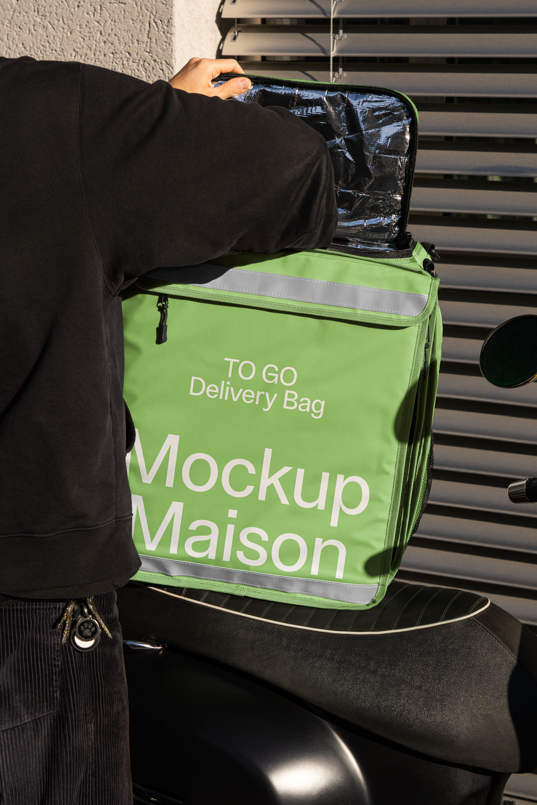 PSD mockup of a person opening a green delivery bag labeled "Mockup Maison" on the back of a scooter, with sunlight casting shadows.