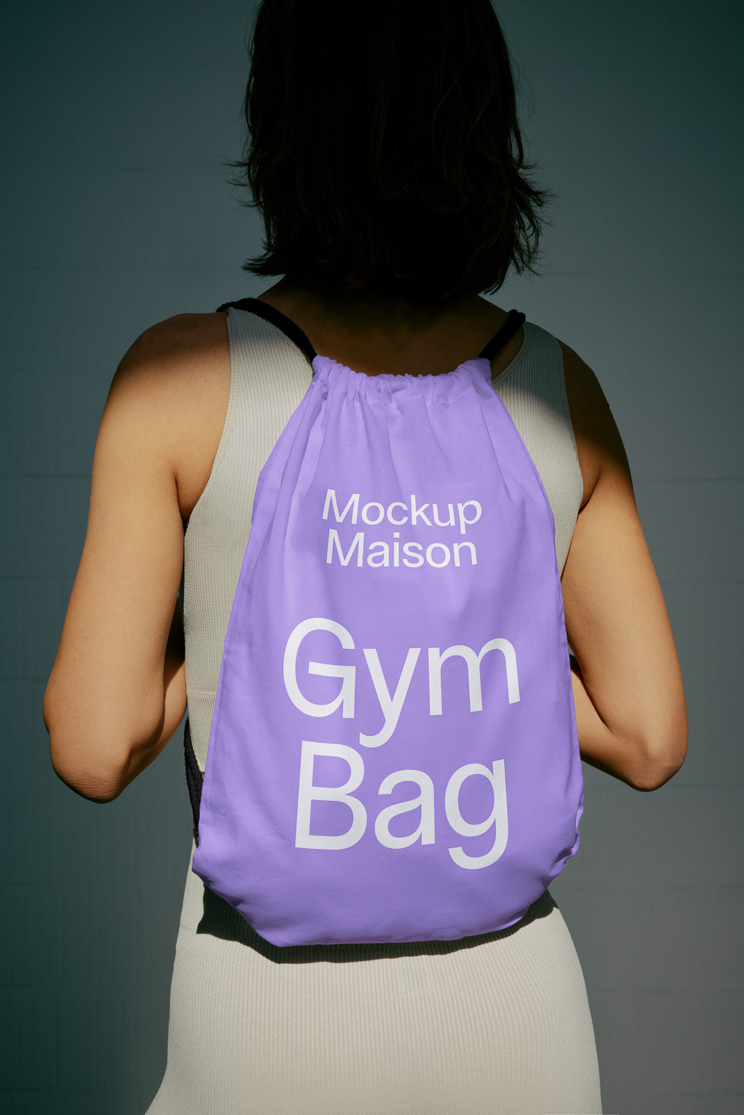 PSD mockup of a lavender gym bag worn by a person in a sleeveless top, showcasing the text "Mockup Maison Gym Bag" in white letters.