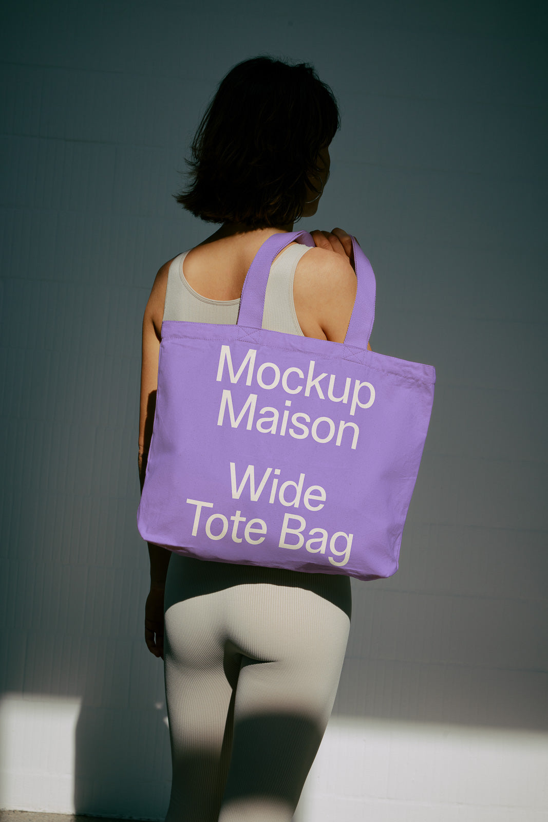 PSD mockup of a purple tote bag with "Mockup Maison Wide Tote Bag" text, carried by a person in a light-colored outfit.