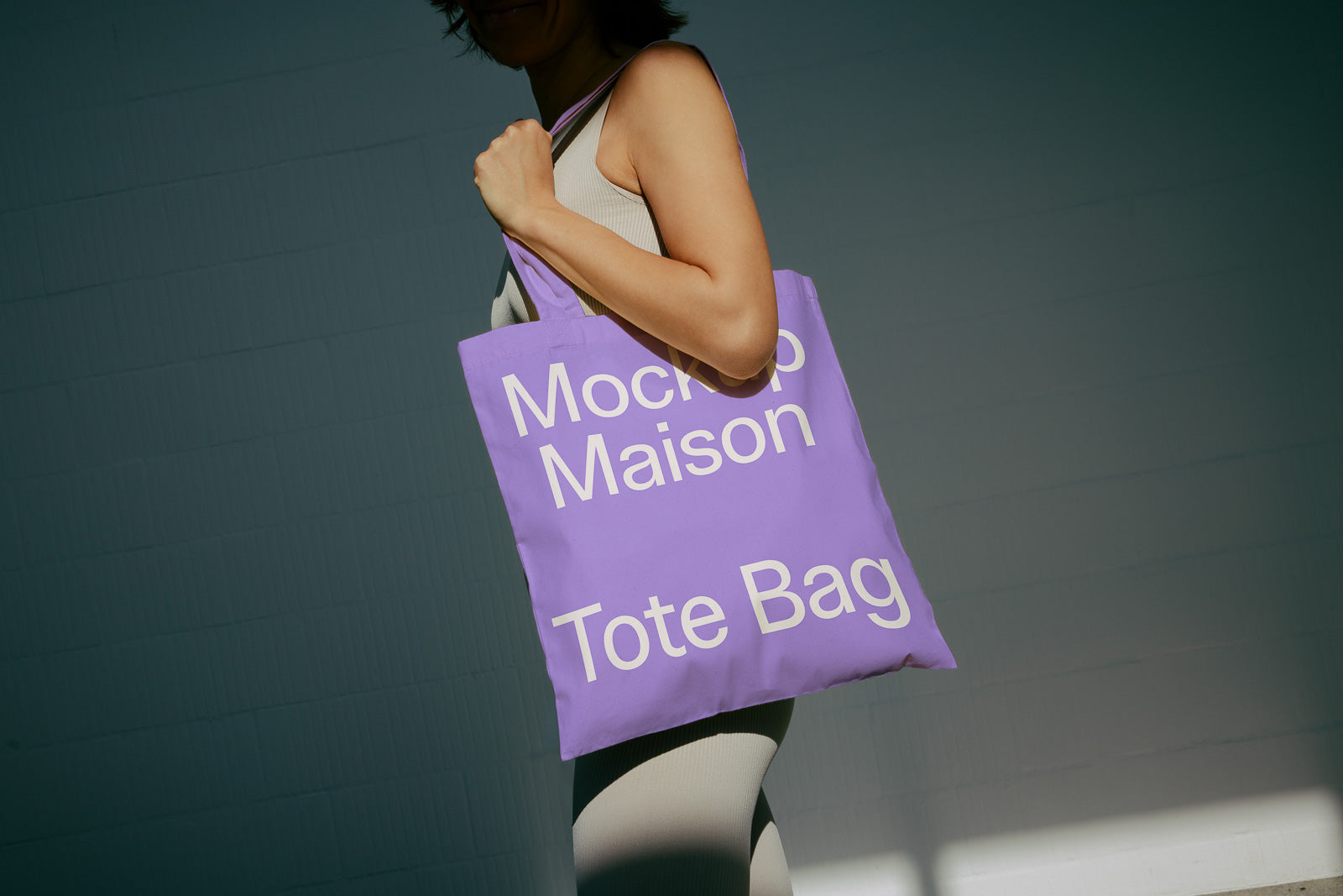 PSD mockup of a person holding a purple tote bag with the text "Mockup Maison Tote Bag" on it, against a neutral background.