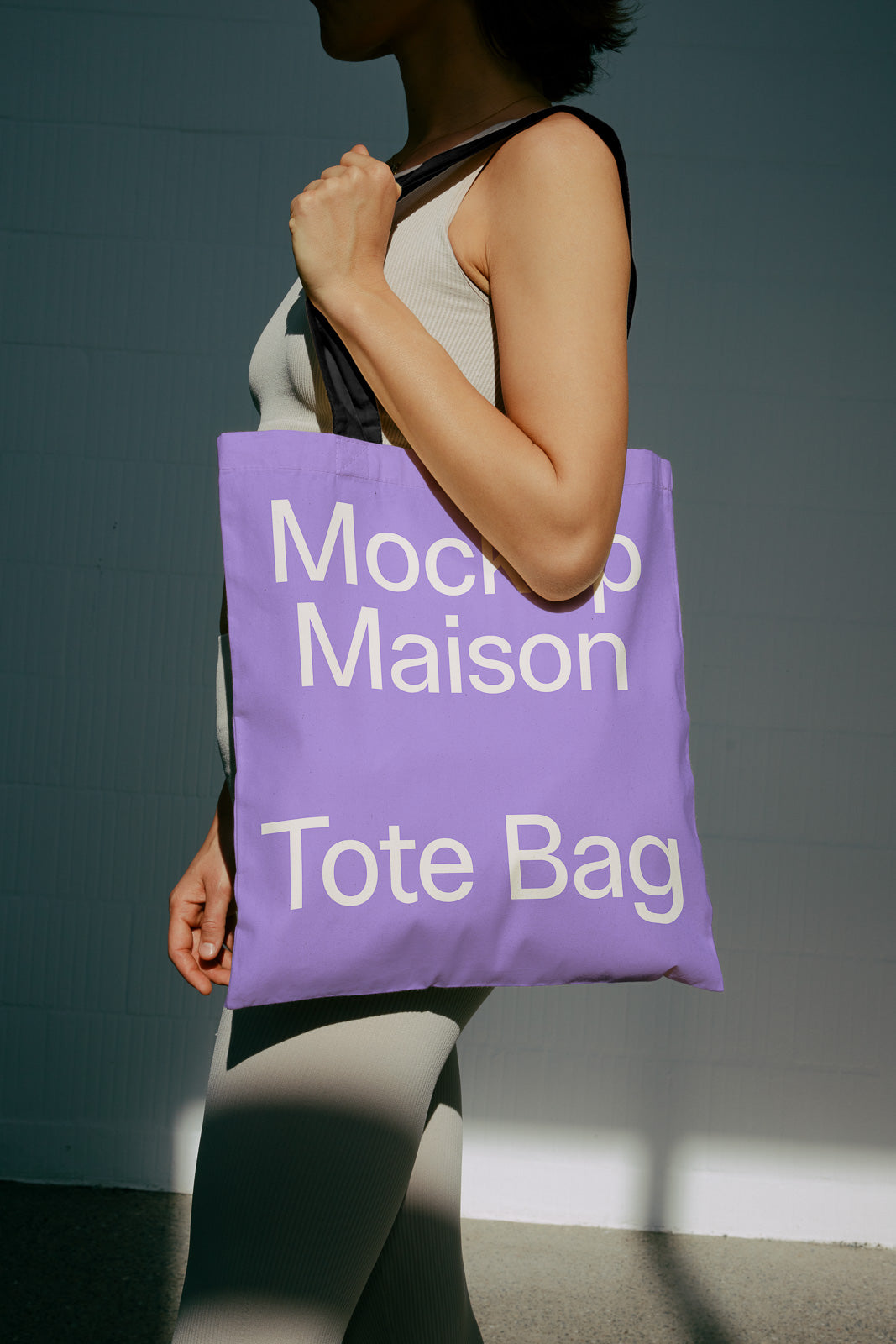PSD mockup of a purple tote bag with white text, worn by a person in a beige outfit, set against a dark background.