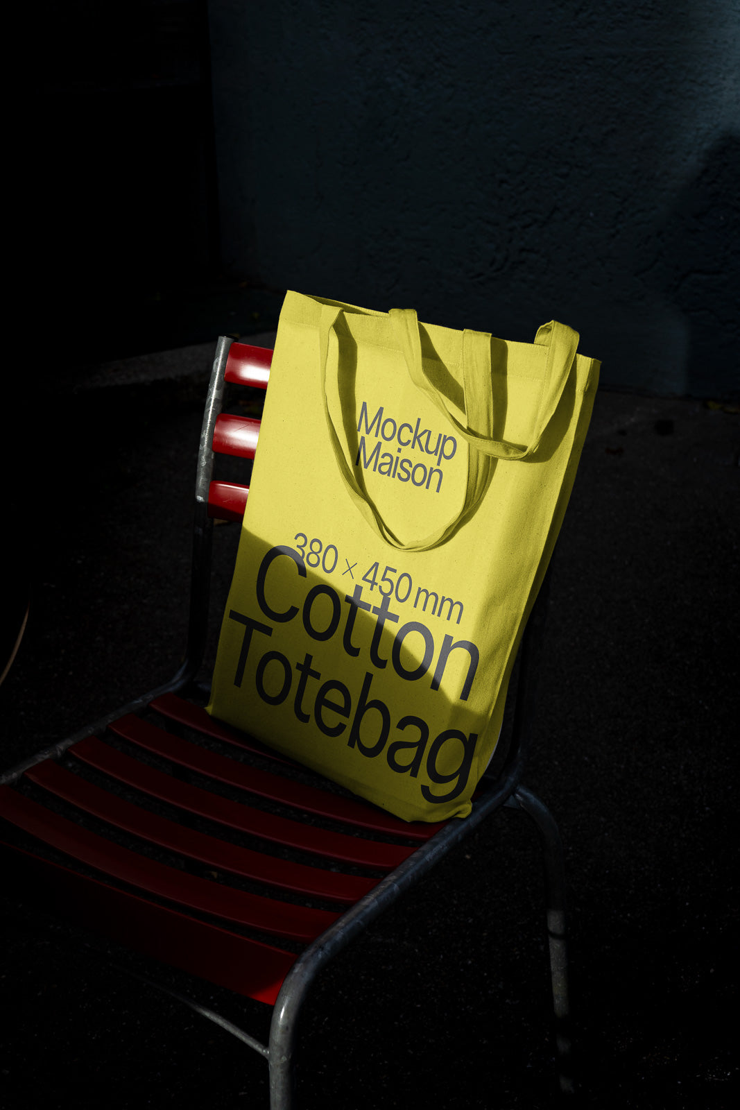 PSD mockup of a yellow cotton tote bag with "Mockup Maison" and dimensions written on it, placed on a red slatted chair.
