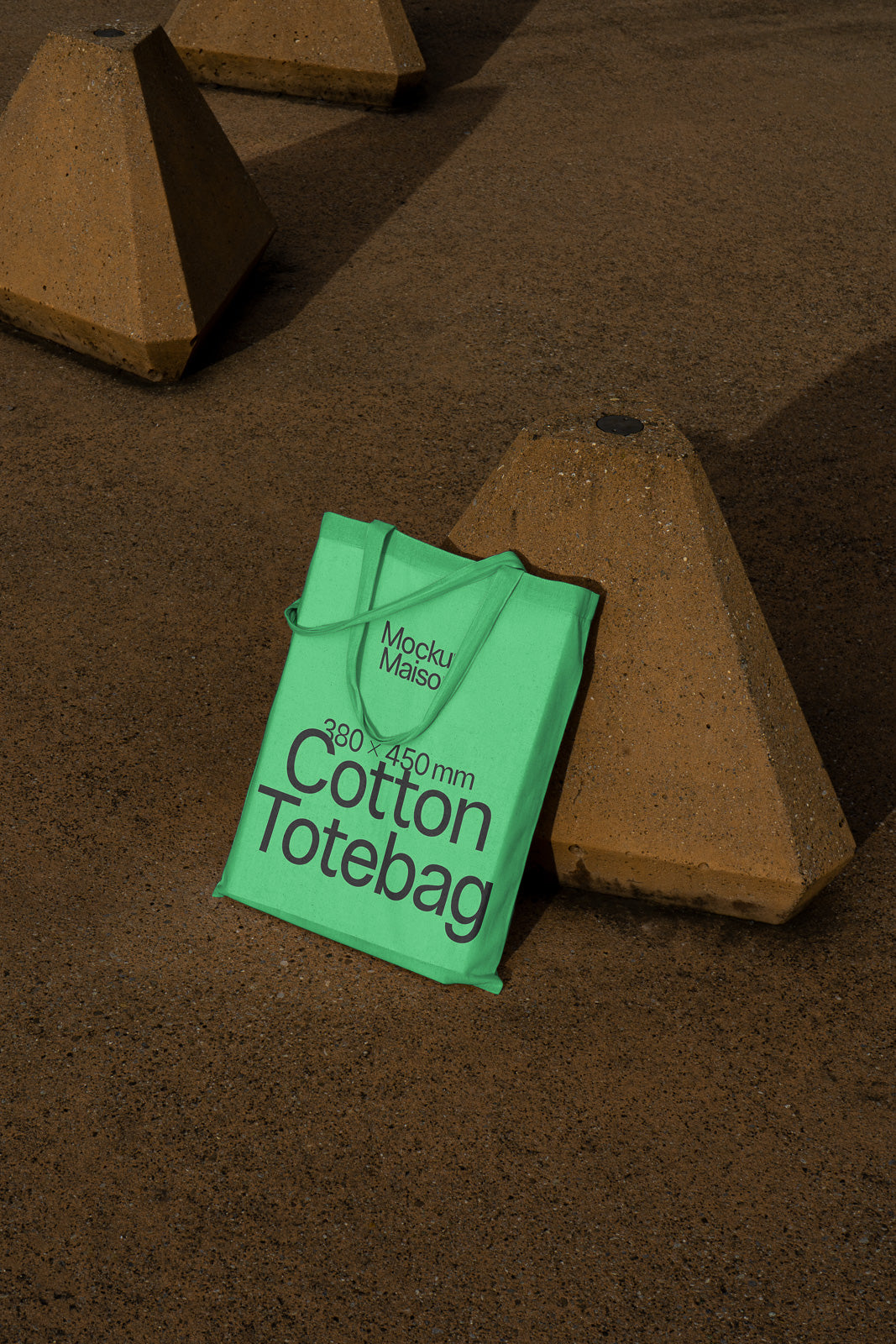 PSD mockup of a green cotton tote bag with dimensions 380 x 450 mm, placed against geometric concrete shapes on a textured surface.