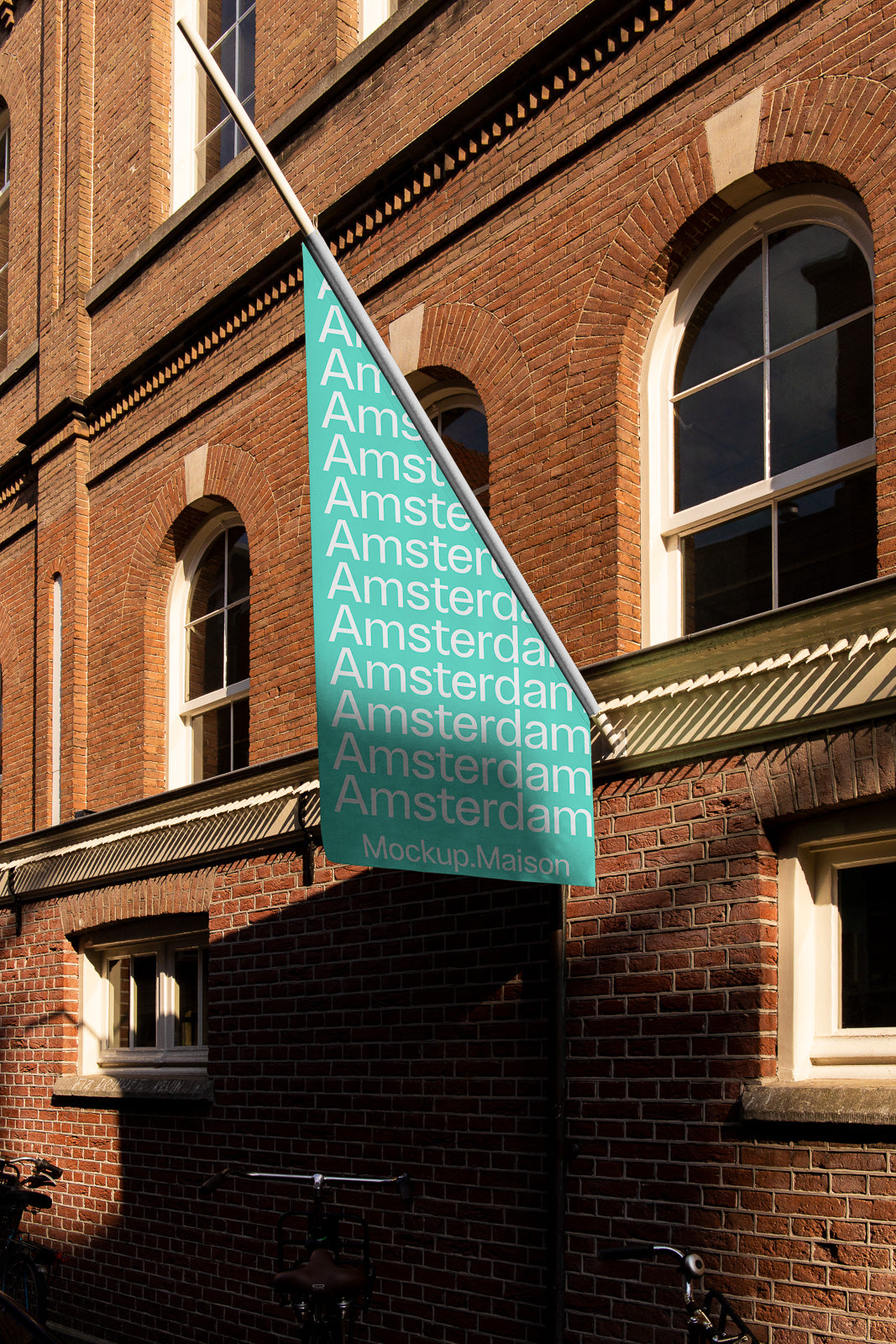 PSD mockup of a teal flag displaying the word "Amsterdam" multiple times, attached to a brick building with arched windows in sunlight.