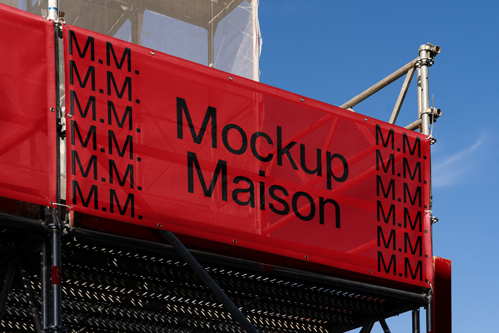 PSD mockup of a red banner with "Mockup Maison" and "M.M." text arranged in multiple columns on a metal scaffold against a clear blue sky.